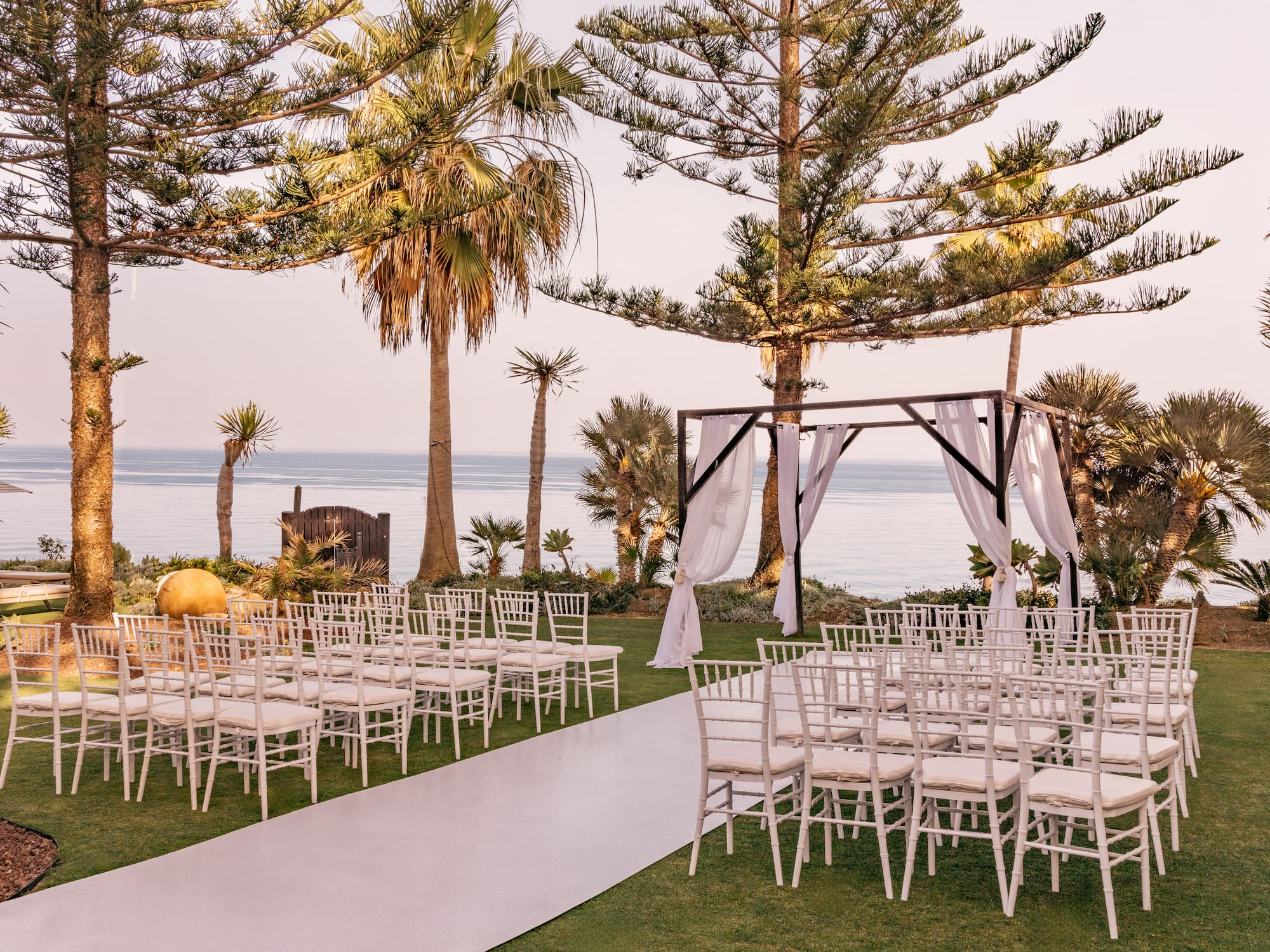 Oceanfront wedding ceremony with white chairs, arch, and palm trees.