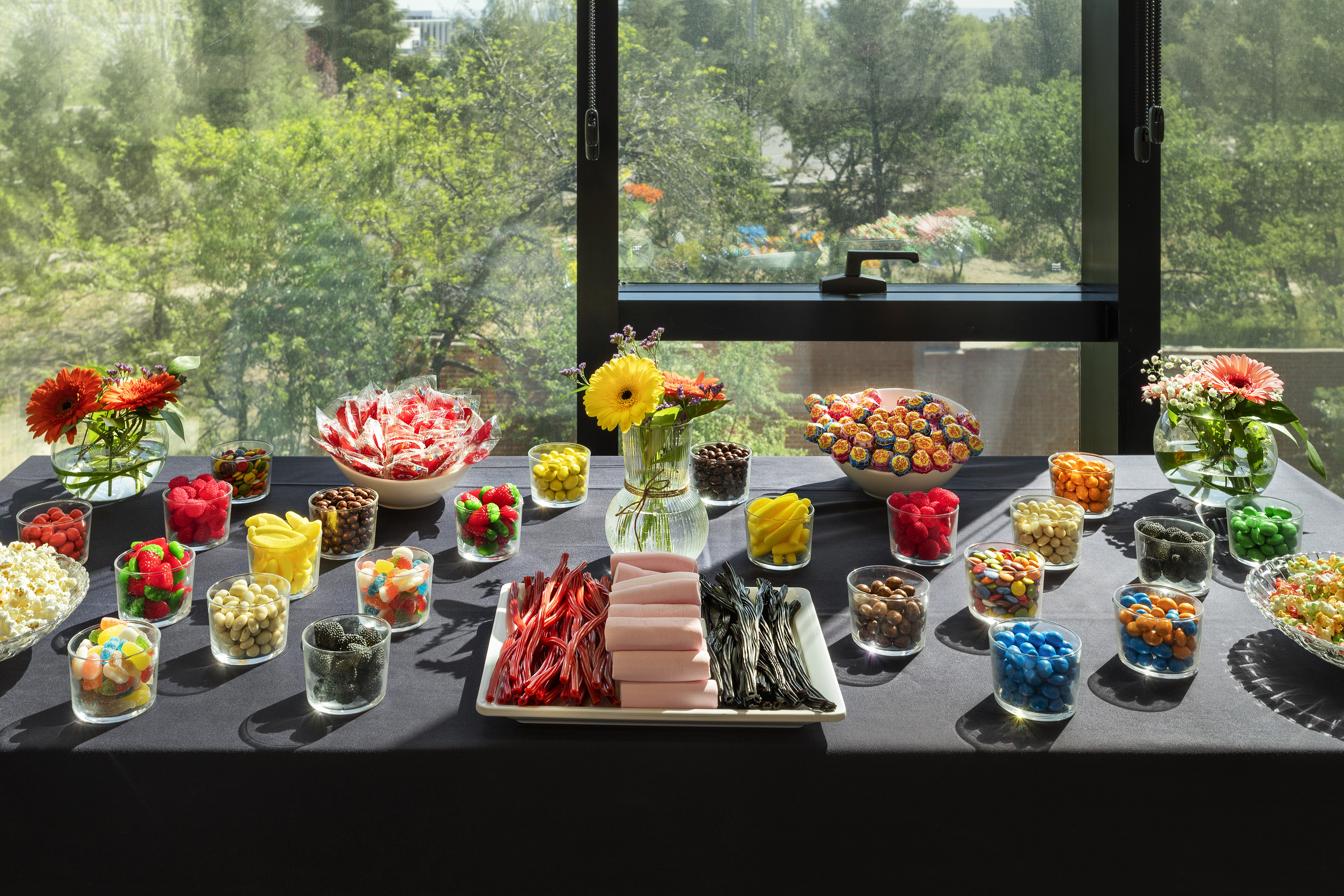 Colorful candy buffet with assorted sweets and flowers on table, window view.