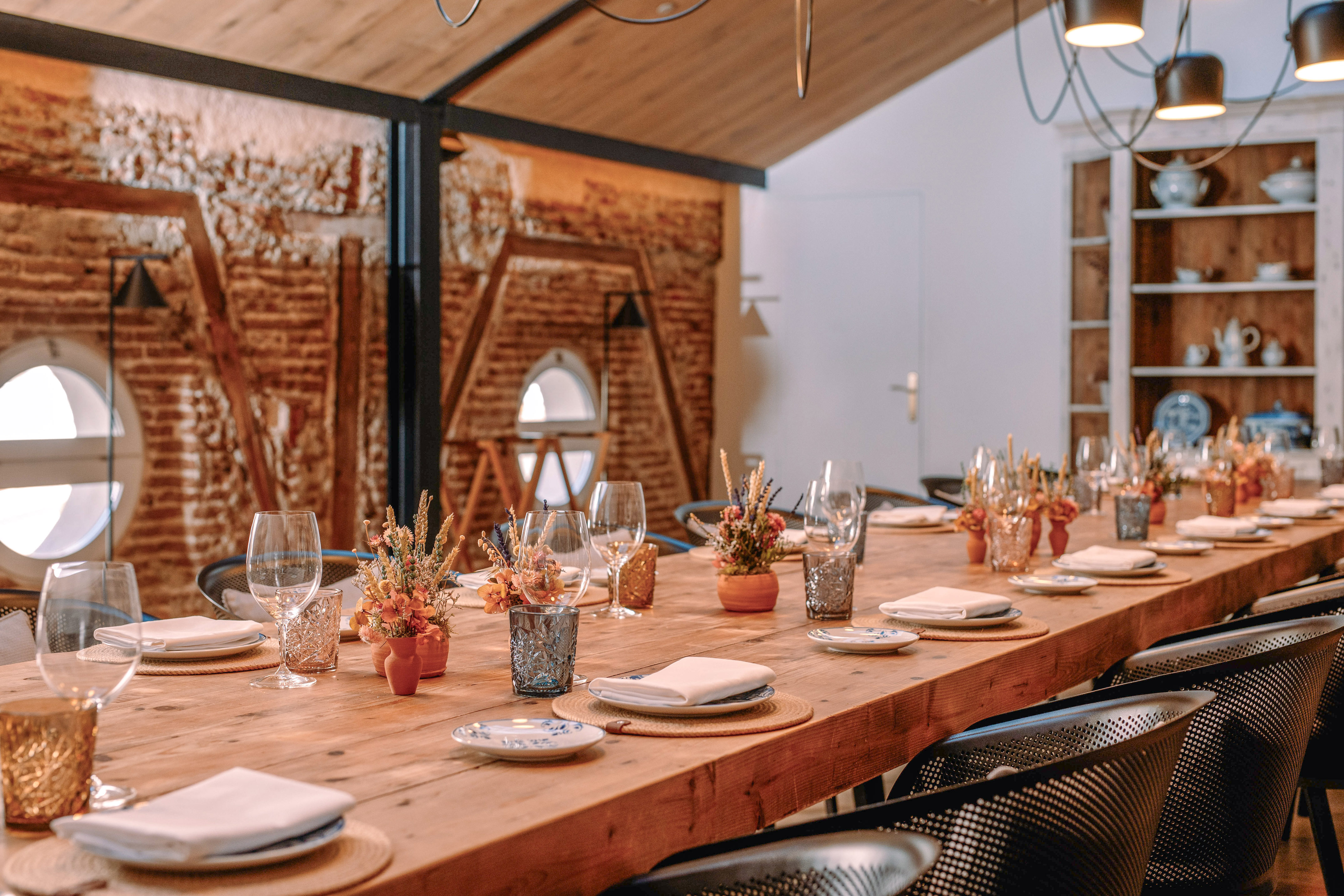 Rustic interior with exposed brick, wooden ceiling, modern chandelier, and hutch.