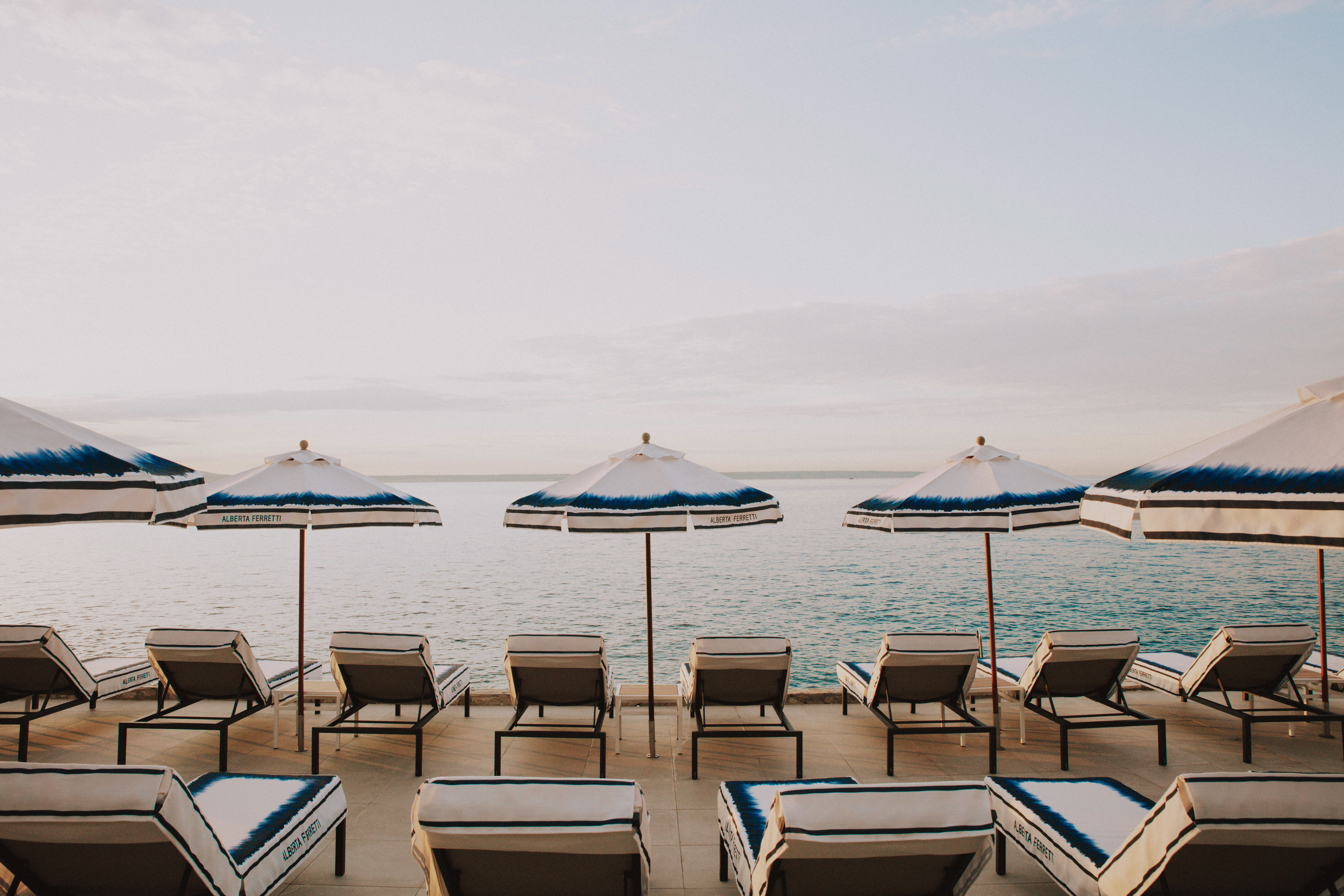 Alberta Ferretti lounge chairs and blue umbrellas on a waterfront patio.