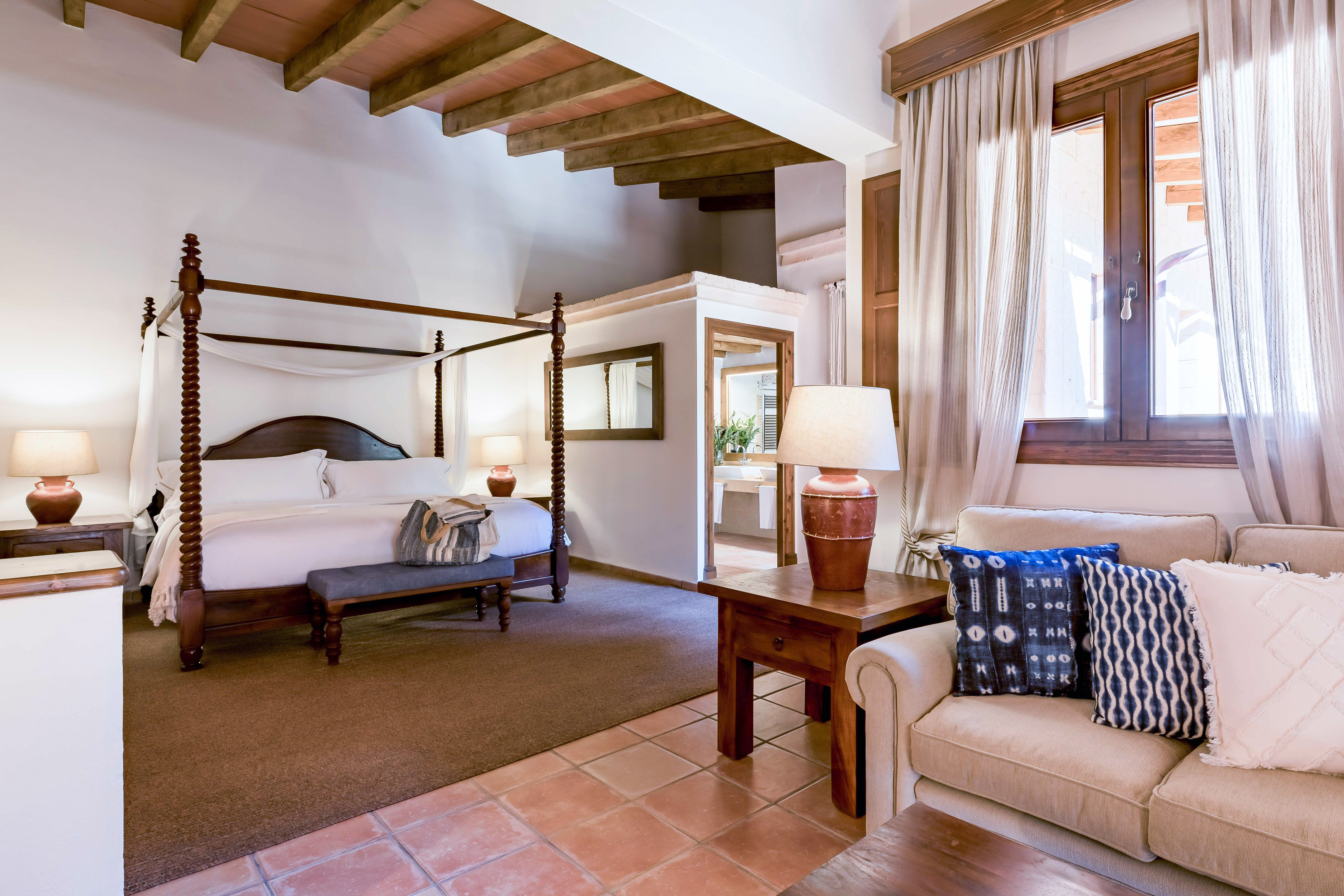 Mediterranean hotel suite with four-poster bed, wooden beams, and terracotta floor.