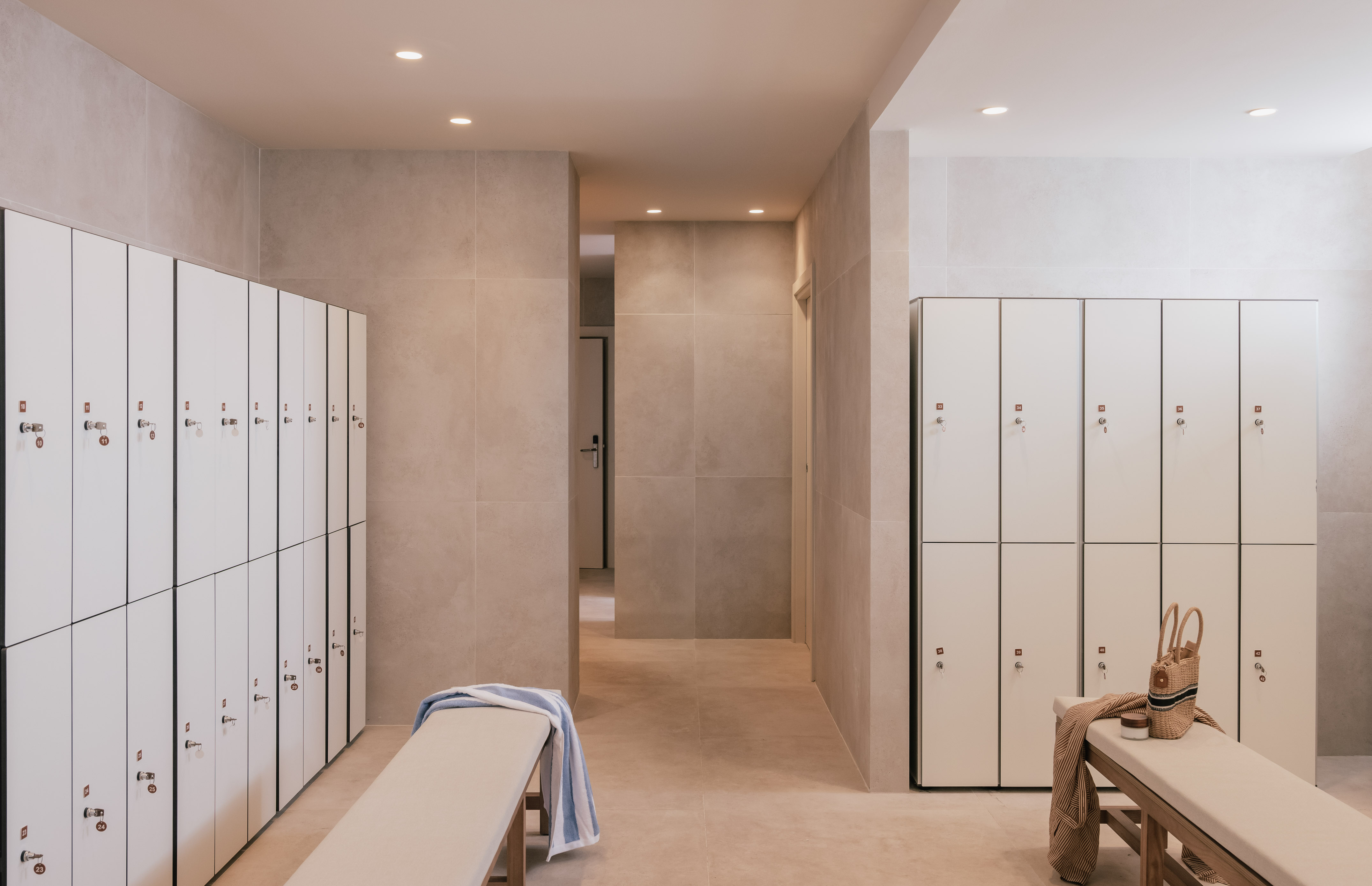 Modern spa changing room with white lockers, benches, and clean tiled interior.
