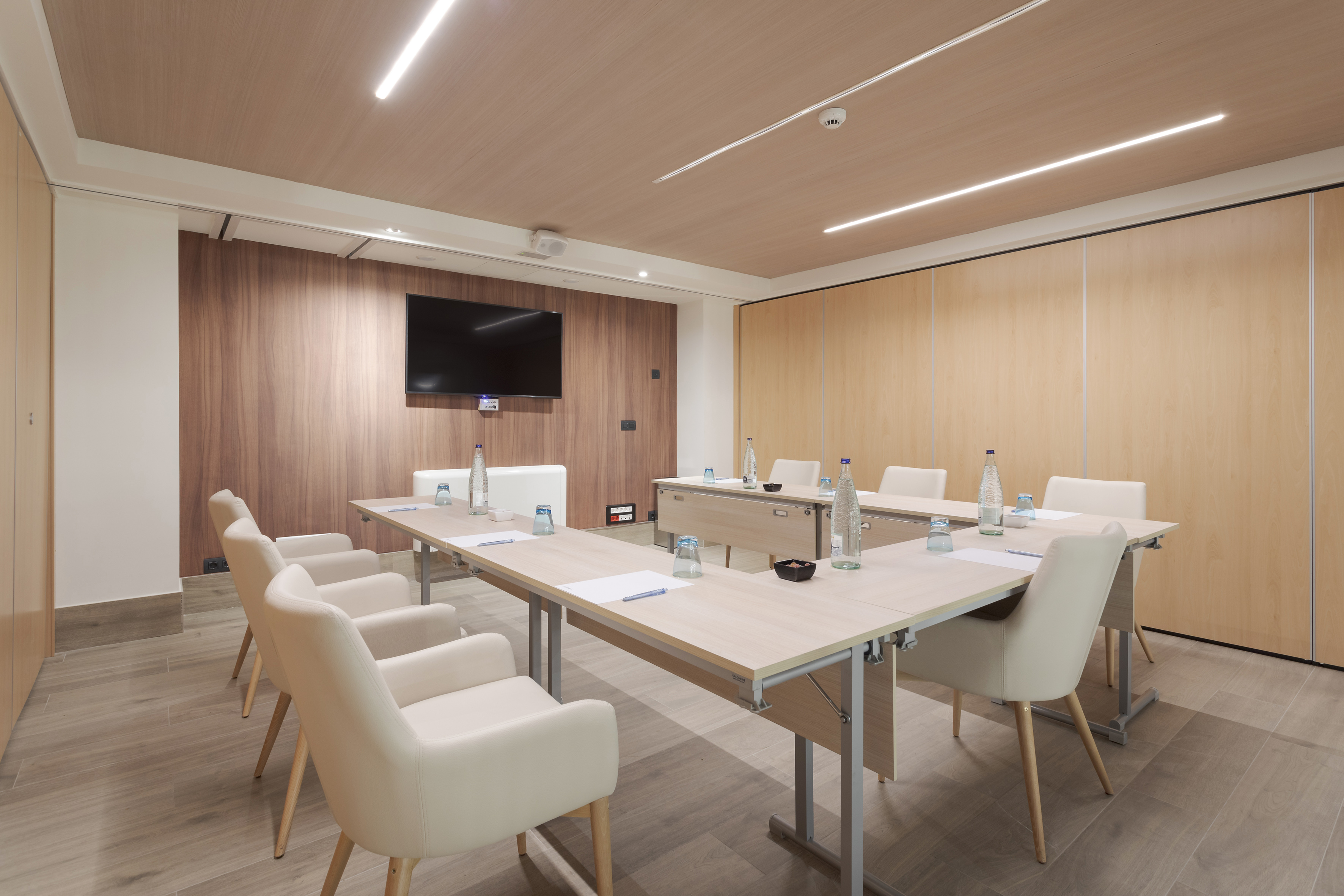 Empty modern conference room with large screen, wood panel walls, and cream chairs.