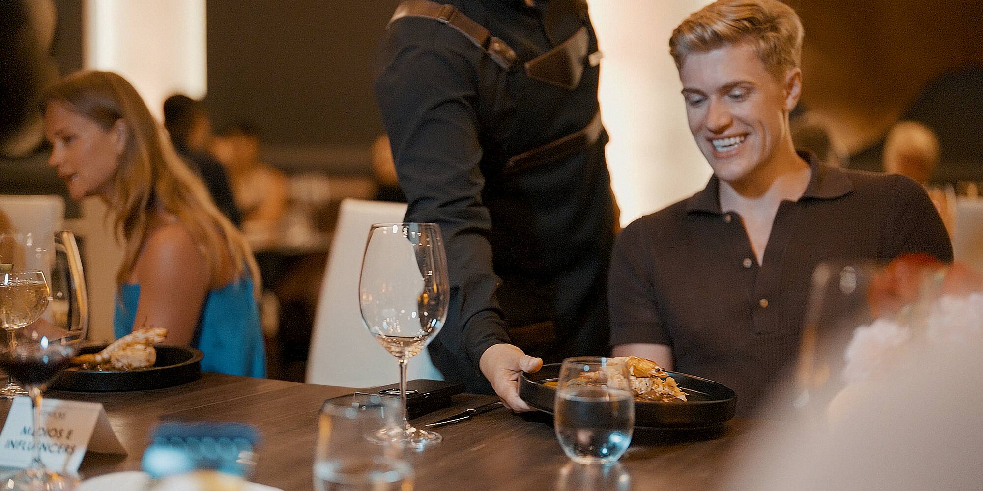 Server brings shrimp dish to a smiling man at an influencer dining event.