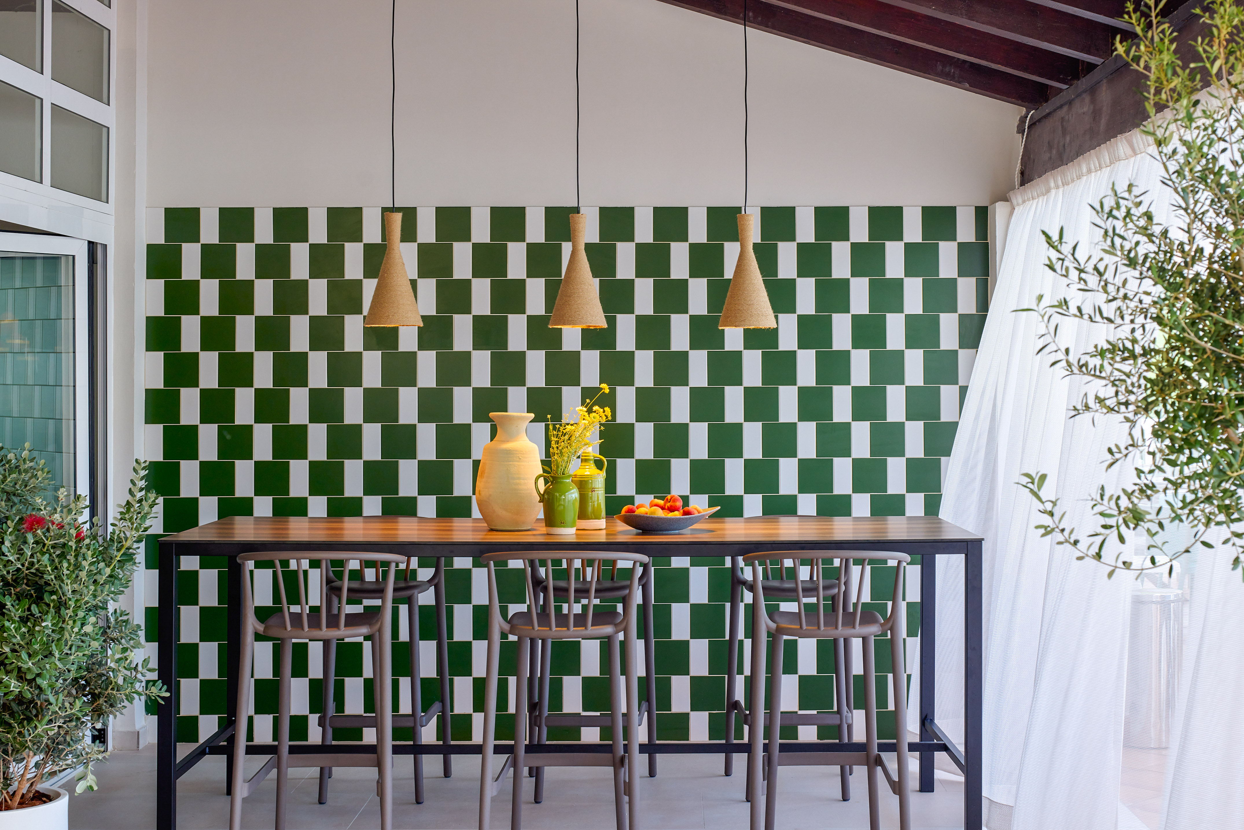 Stylish patio bar with green checkered tiles, wood table, and bar stools.