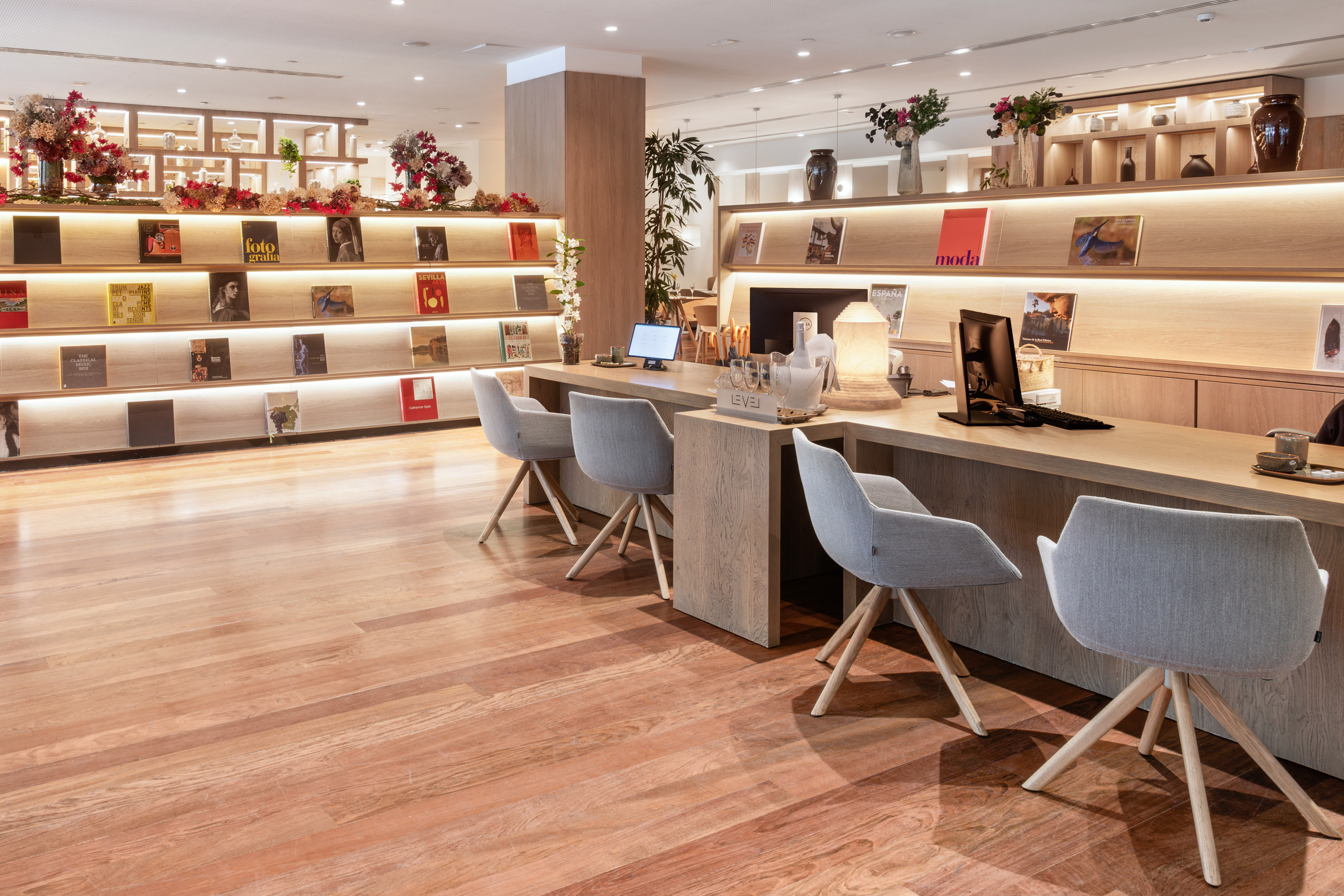Modern hotel lobby desk with grey chairs and illuminated book shelves.