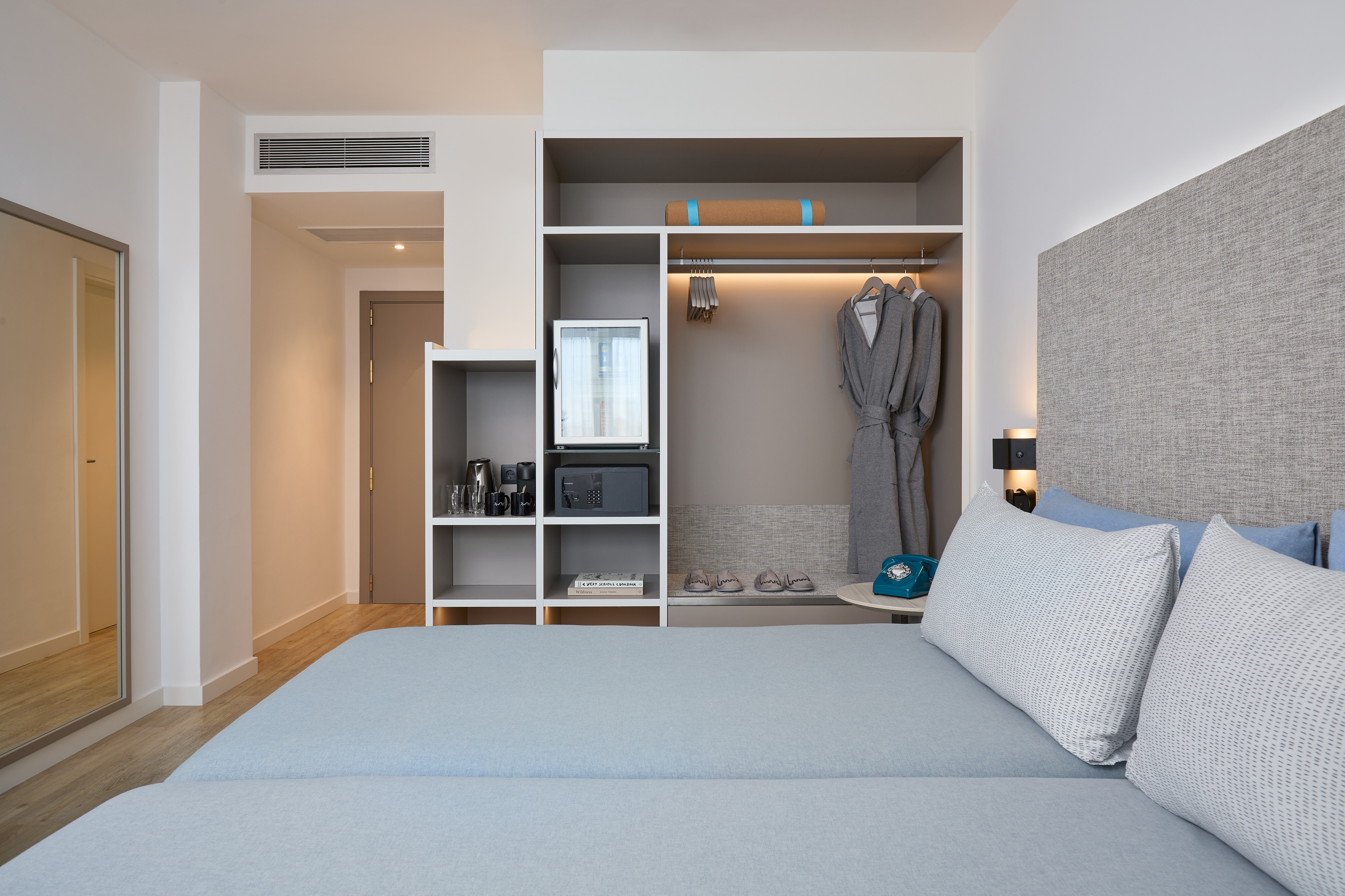 Hotel bedroom with two beds, open wardrobe, mini-fridge, and safe.
