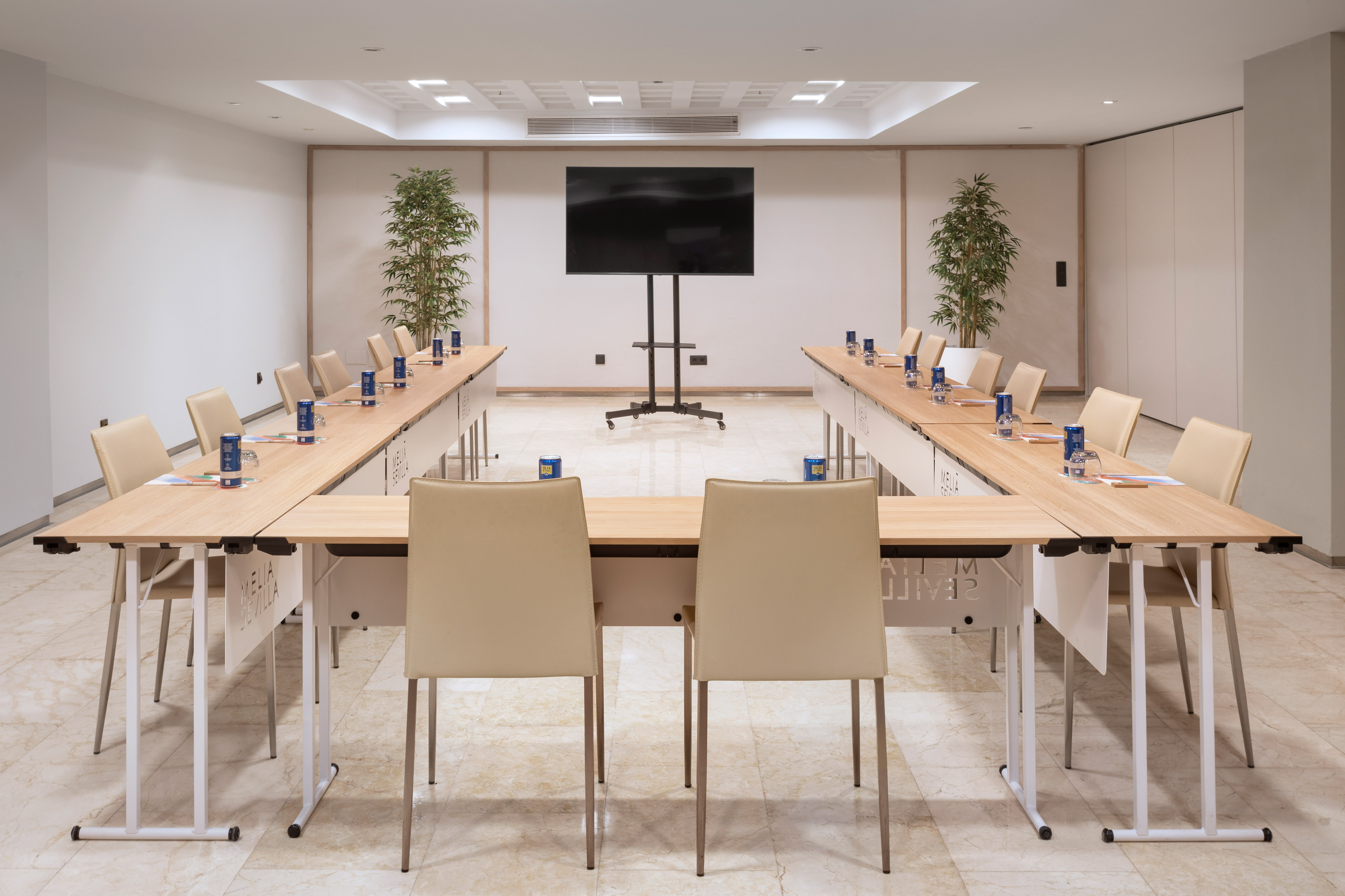 Modern conference room with U-shaped table, beige chairs, and large screen.