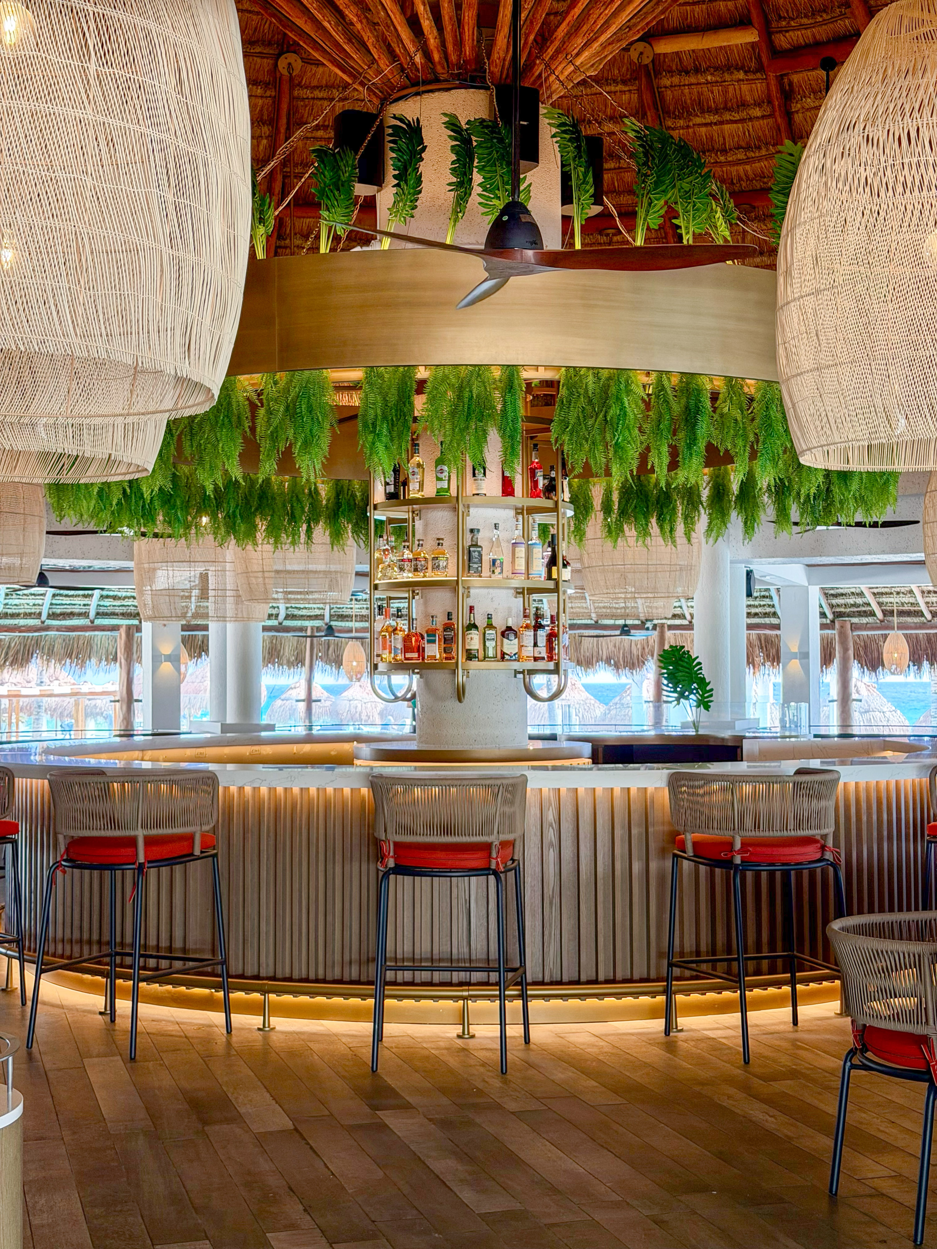 Modern tropical bar with hanging ferns, liquor display, and ocean view.