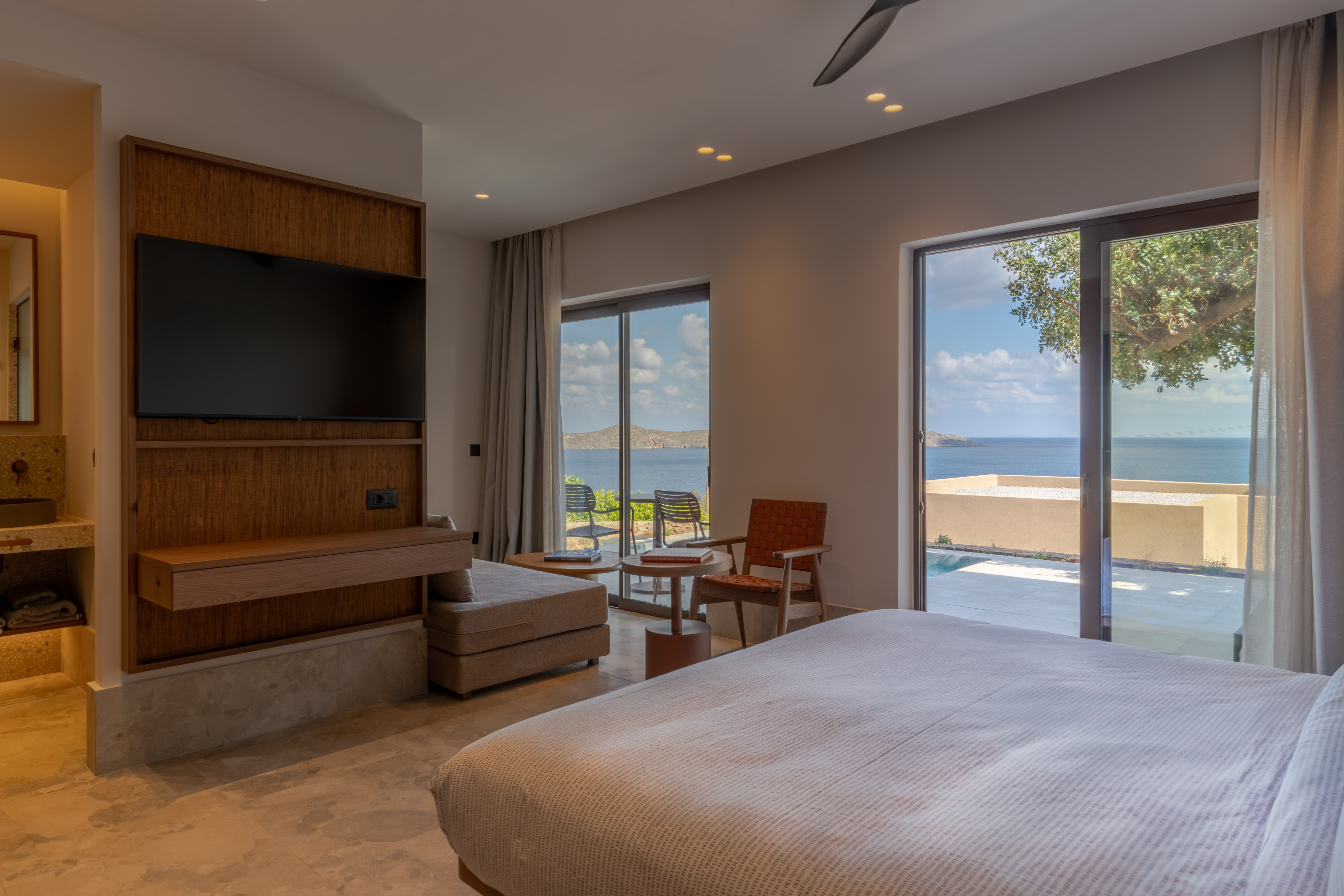 Modern hotel bedroom with sea view, private balcony, pool access, and large bed.