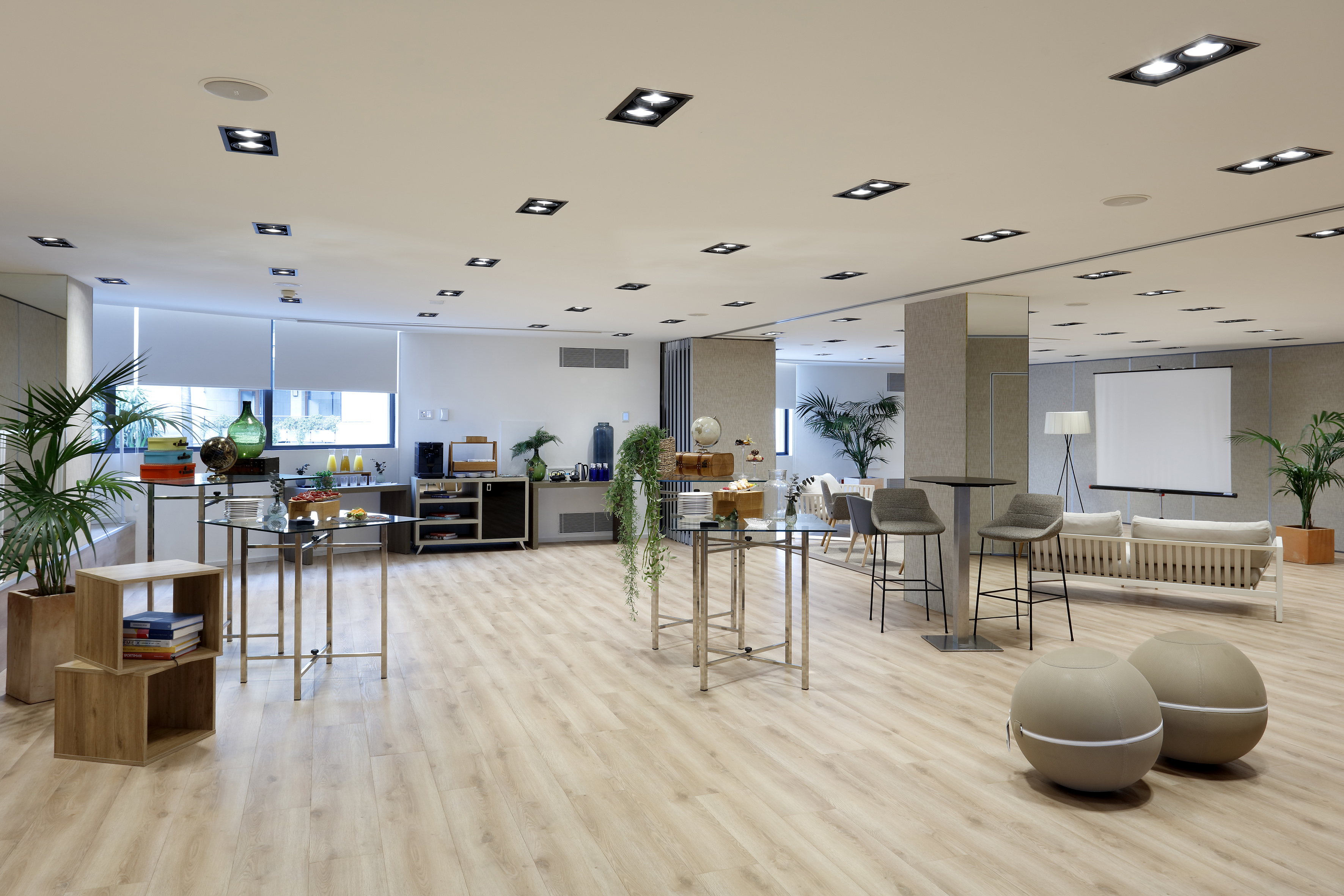 Modern hotel event lounge with buffet, varied seating, and projector screen.