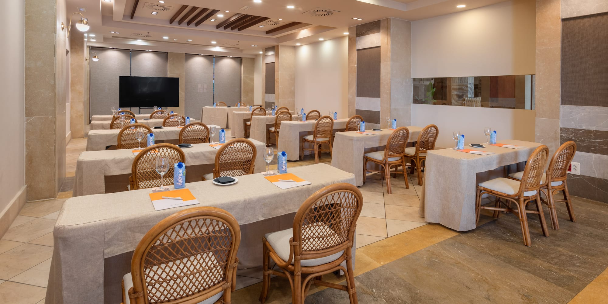 Conference room with tables, wicker chairs, water, and presentation screen.