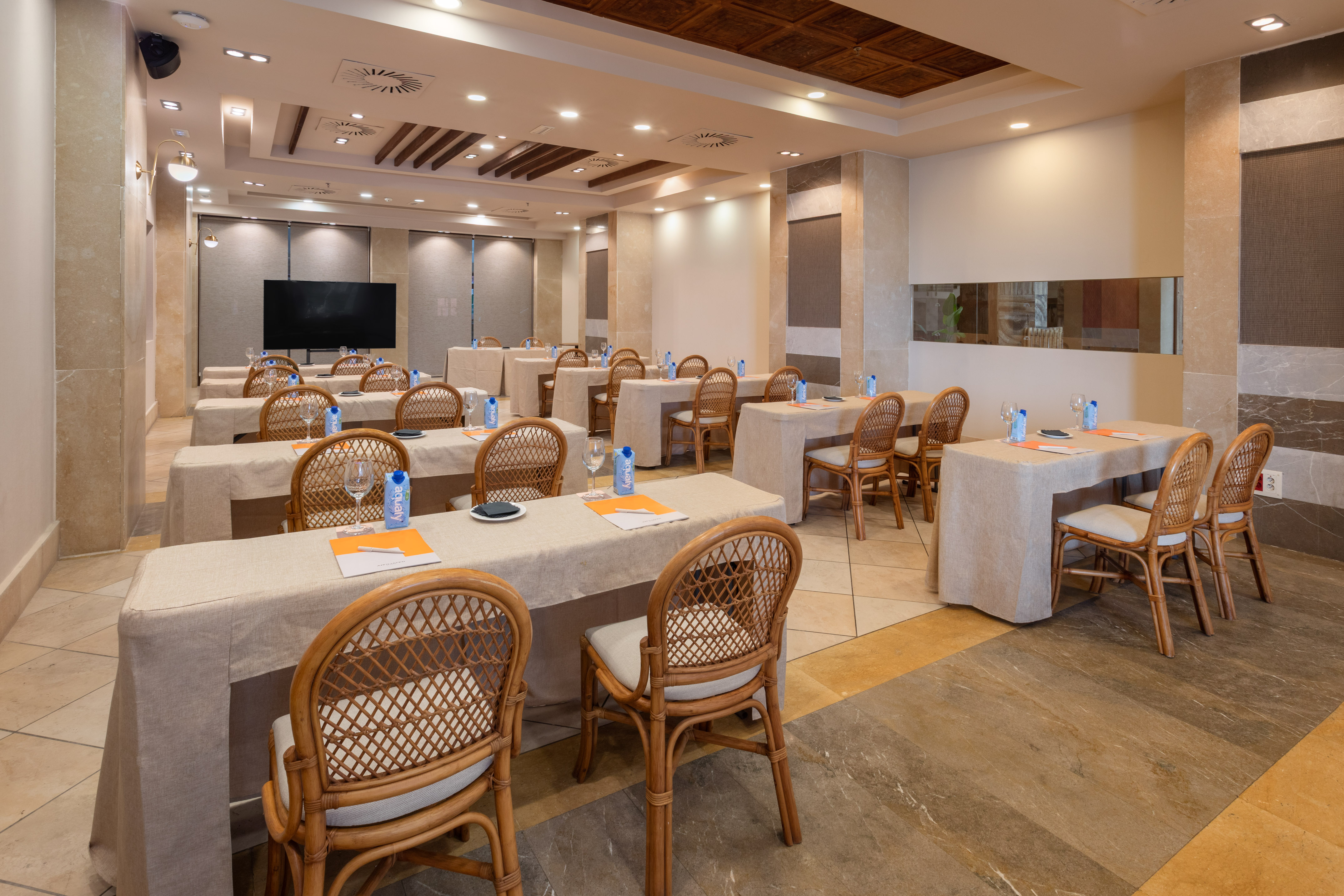 Conference room with tables, wicker chairs, water, and presentation screen.