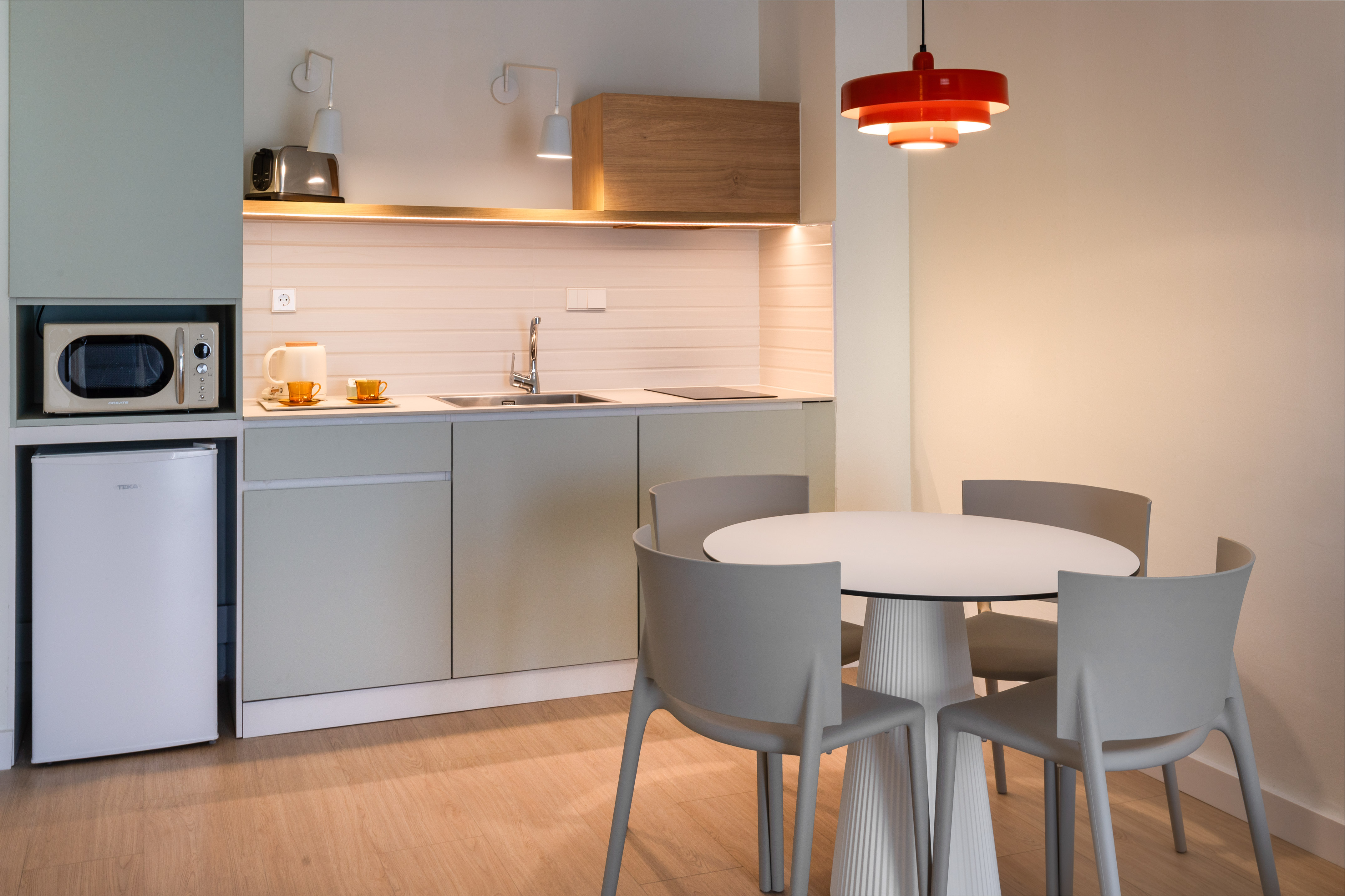 Modern compact kitchen with light green cabinets, appliances, and dining table.