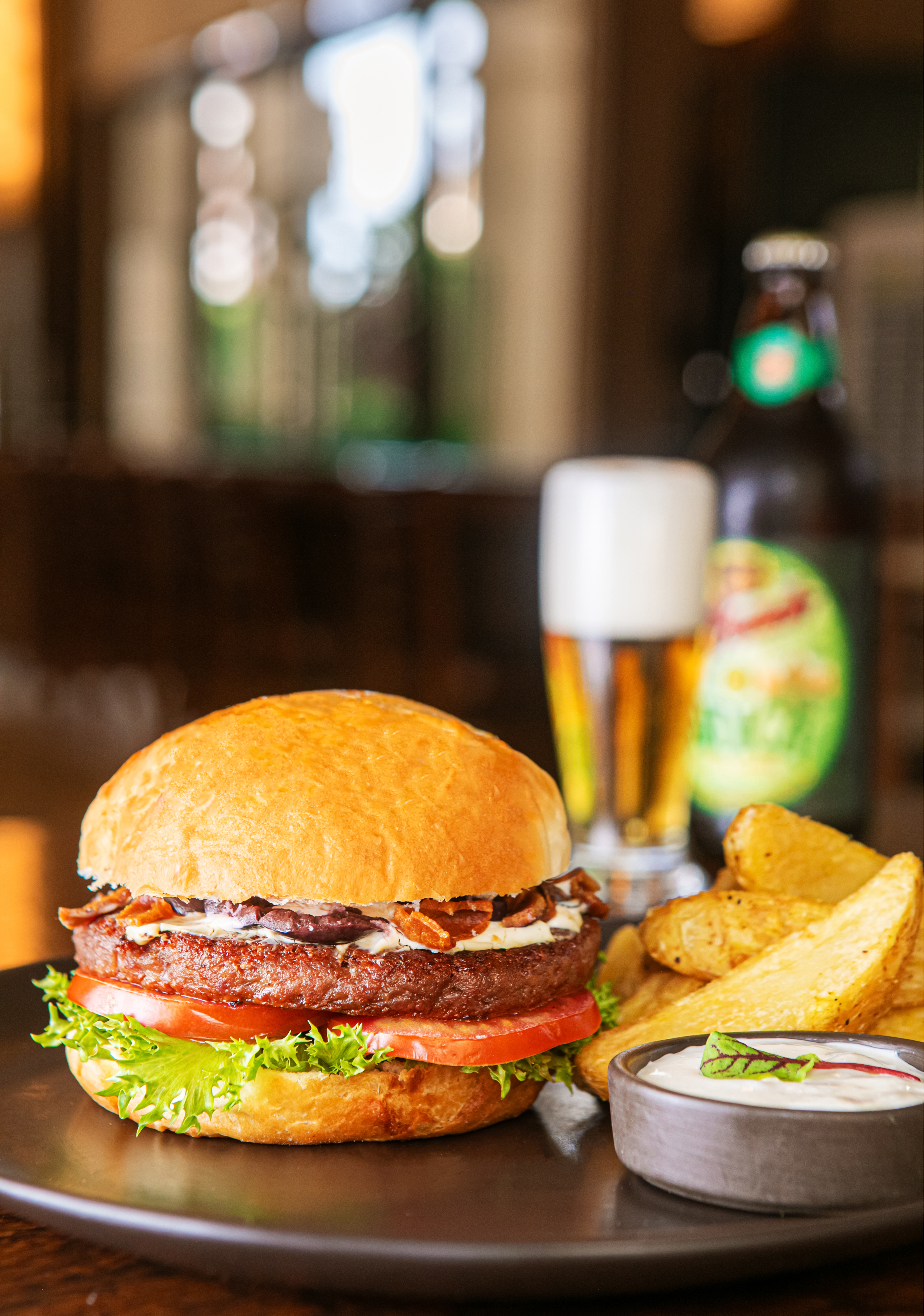 Gourmet burger with bacon, potato wedges, dipping sauce, and beer.