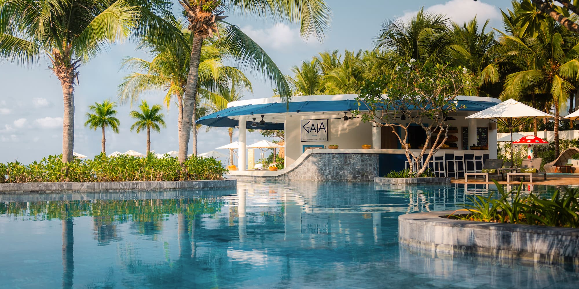 Tropical resort pool with Gaia Mediterranean Pool Bar and lush palm trees.