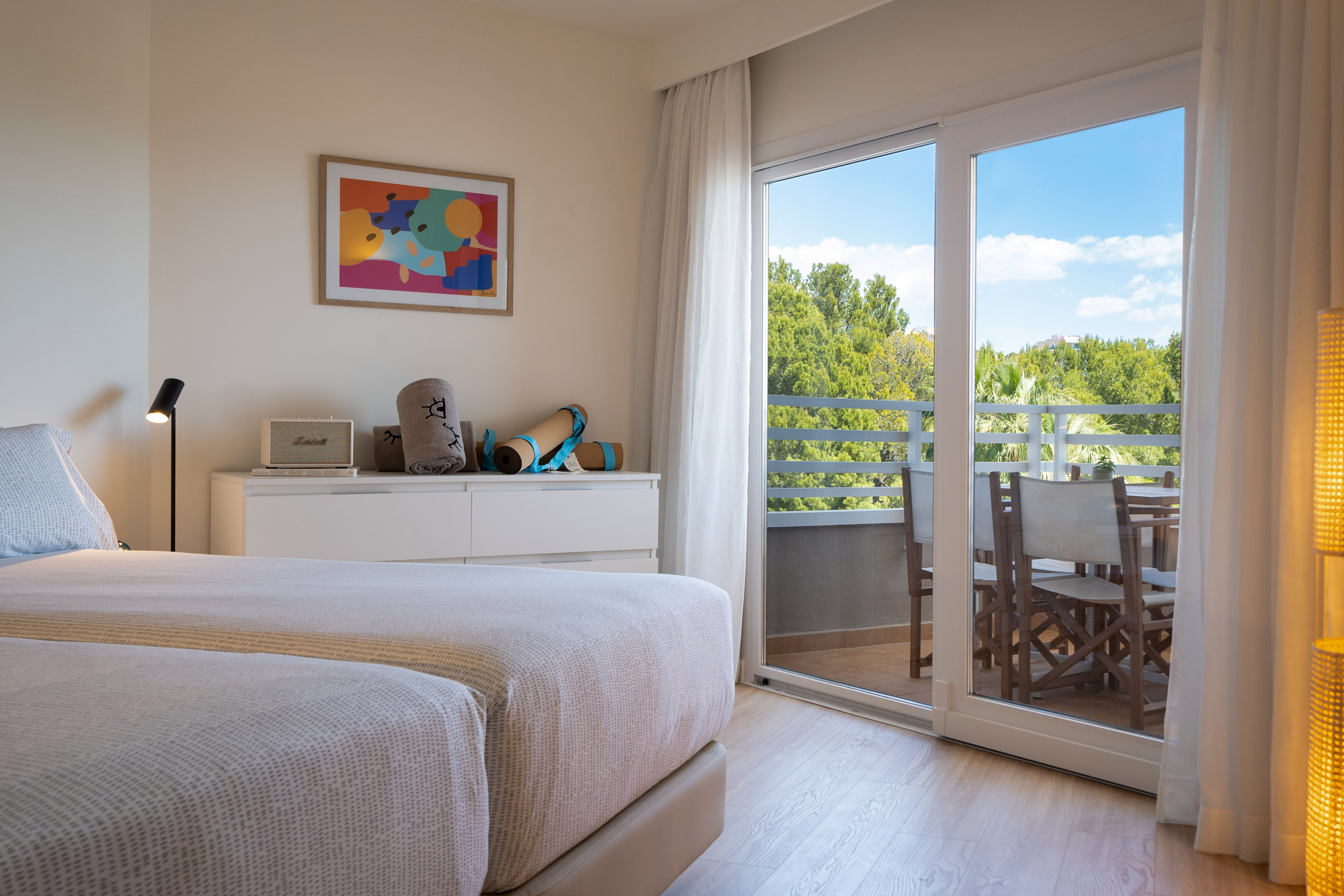 Bright bedroom with twin beds, balcony, forest view, and yoga mats.