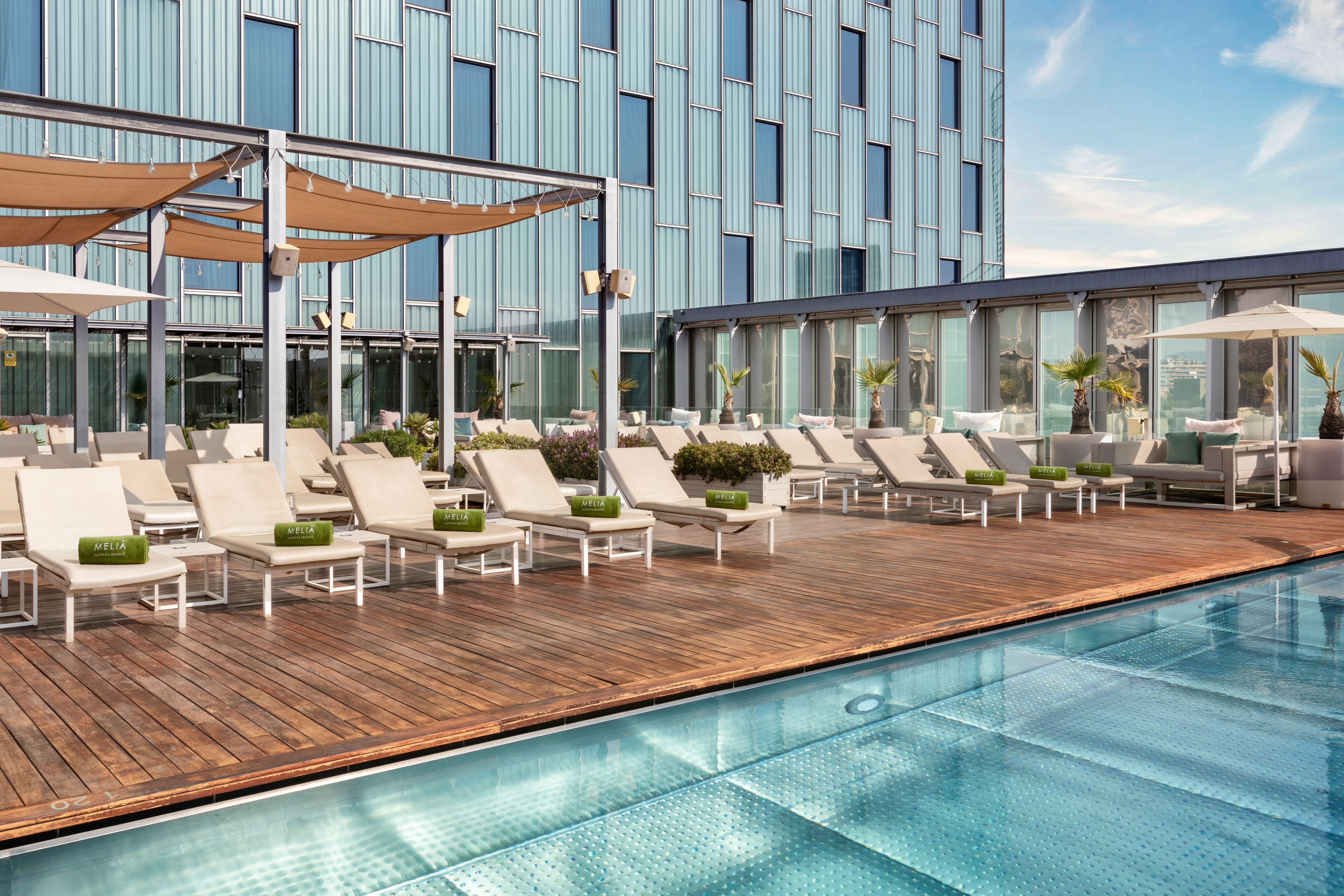 Meliá hotel rooftop pool deck with sun loungers and modern glass building.