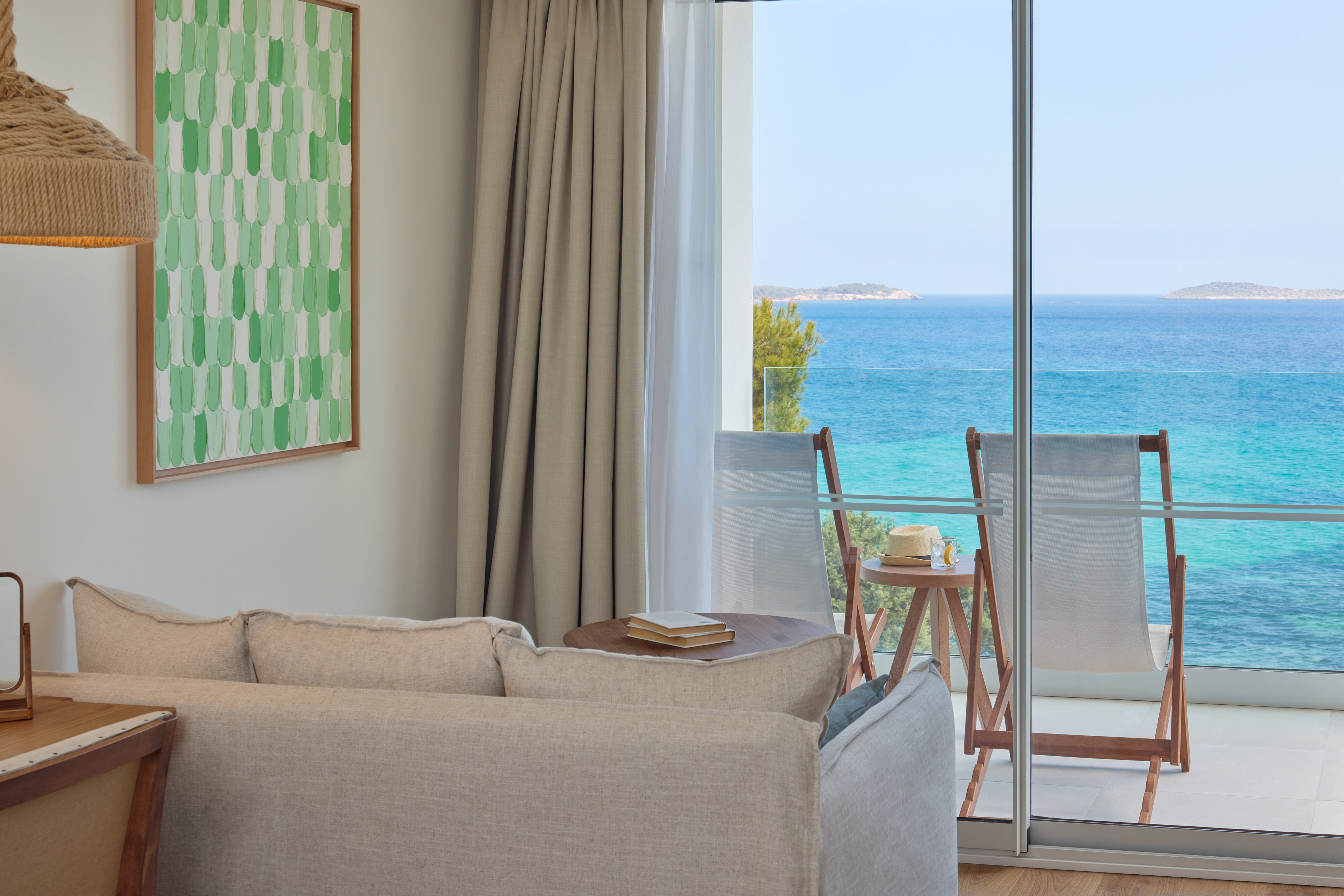 Ocean view room with sofa, balcony, and outdoor lounge chairs by the sea.