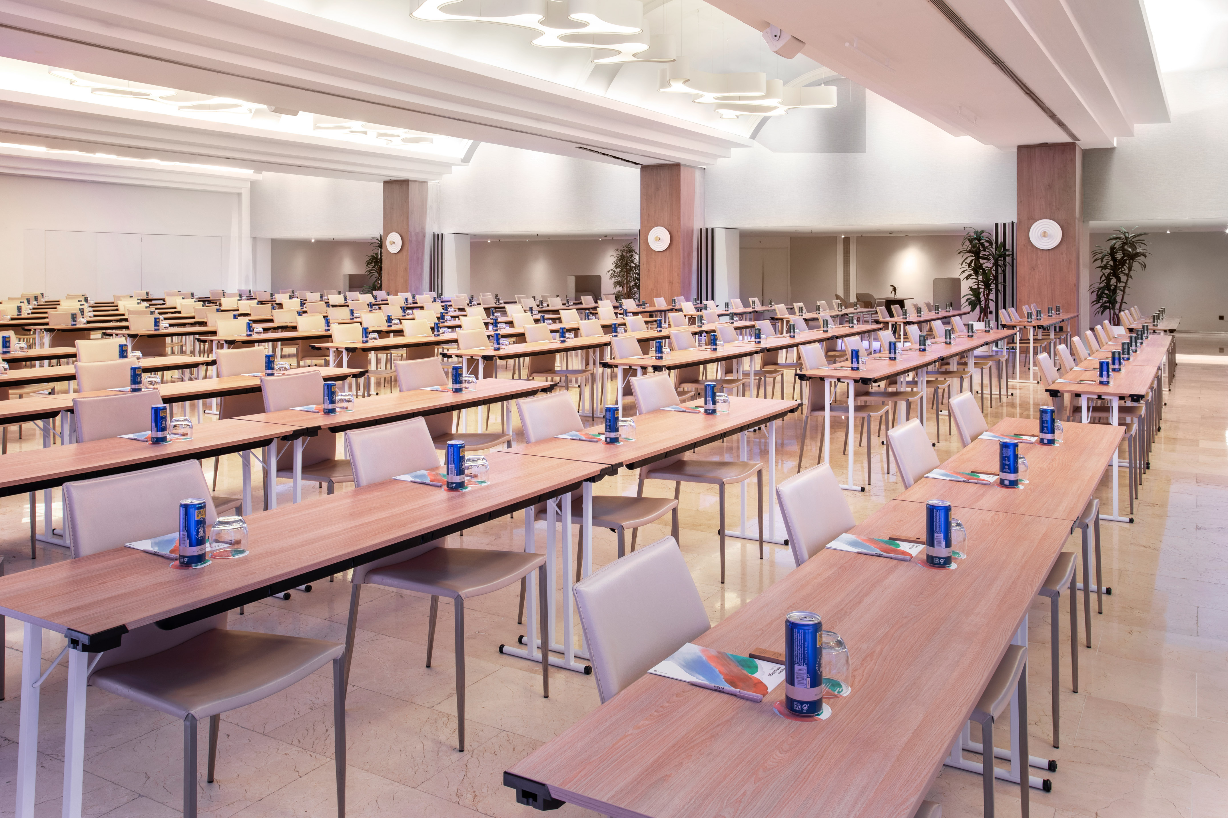 Spacious hotel conference room with rows of tables, chairs, and beverages.