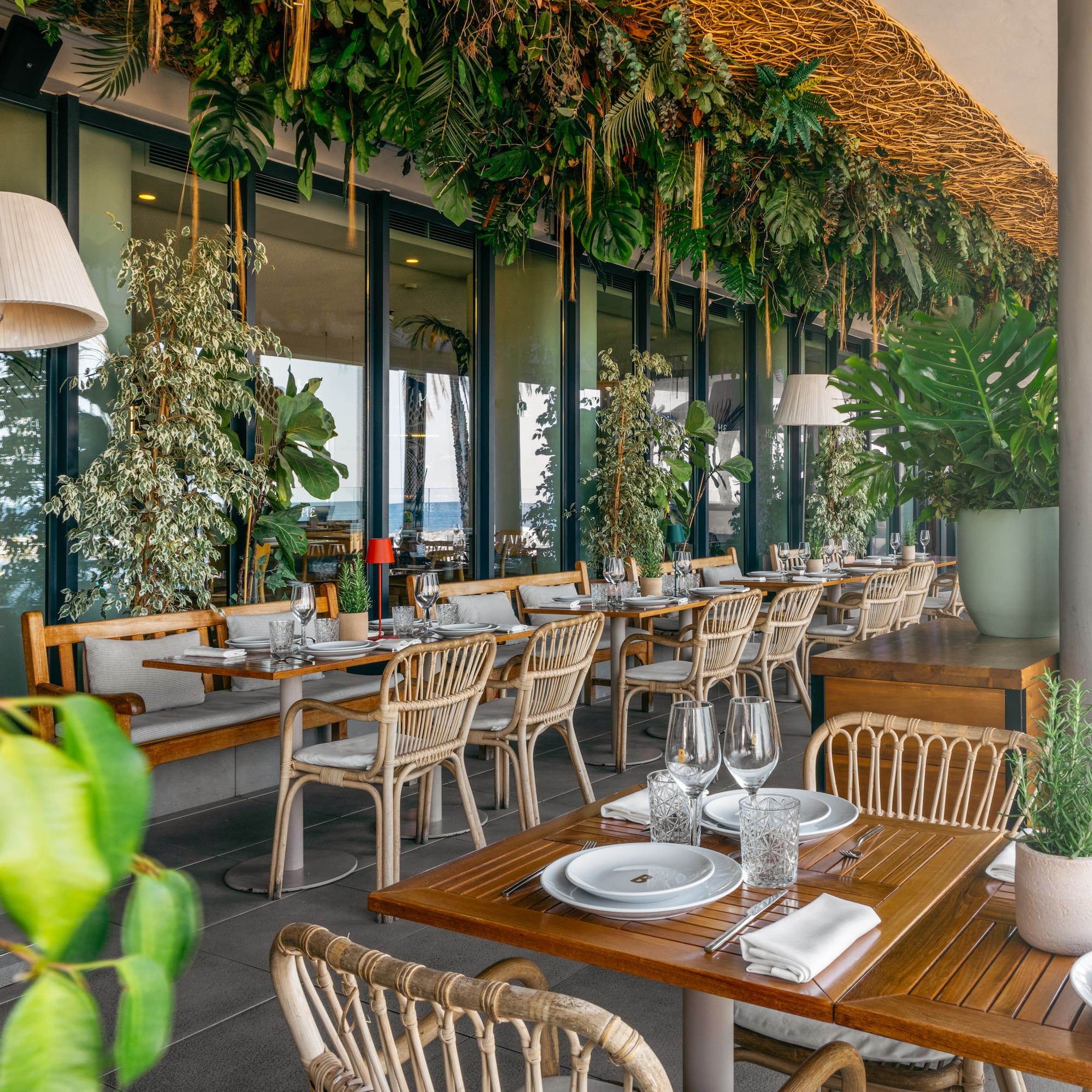 Tropical restaurant patio with lush greenery, wicker seating, and sea views.