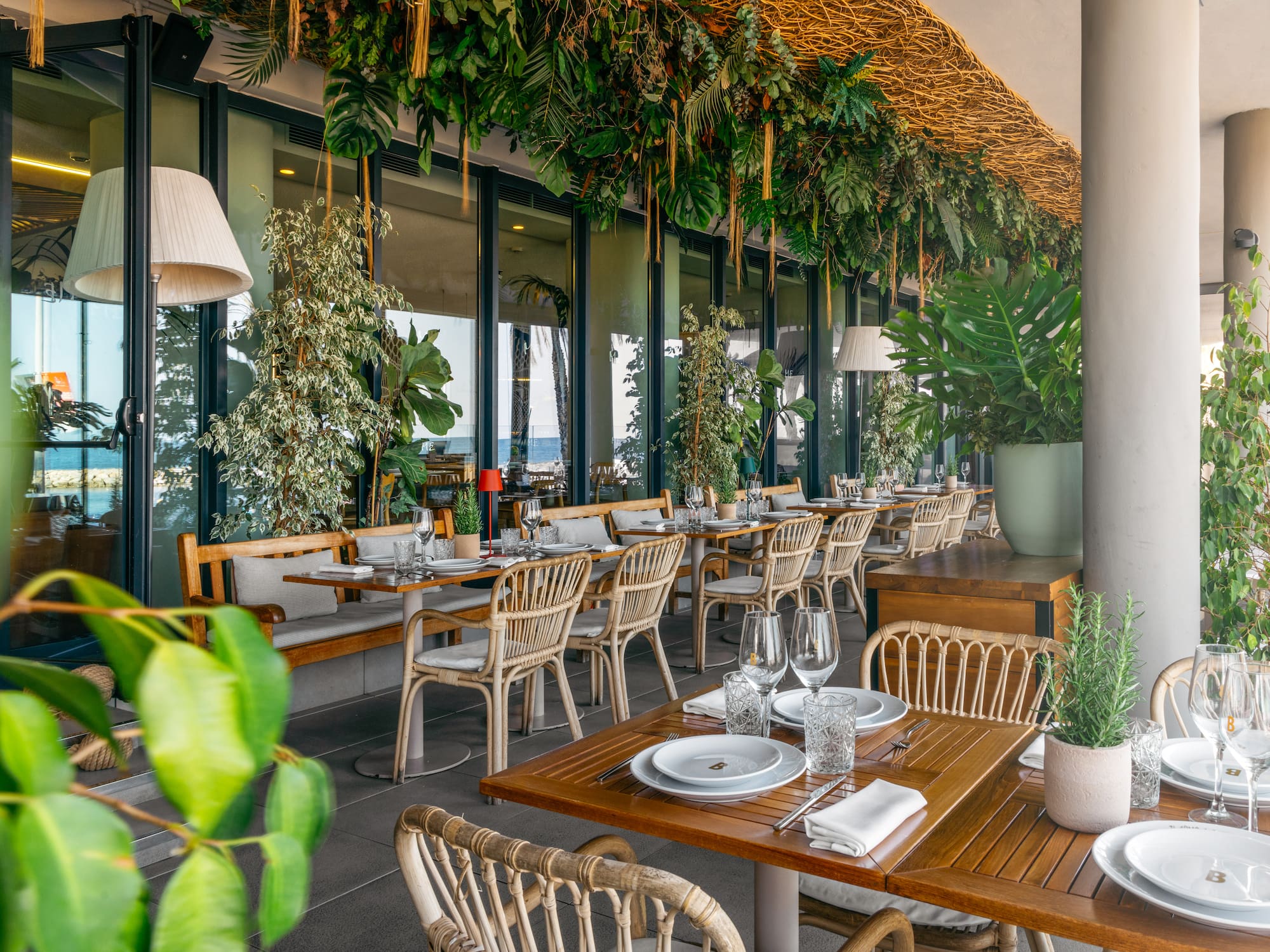 Tropical restaurant patio with lush greenery, wicker seating, and sea views.
