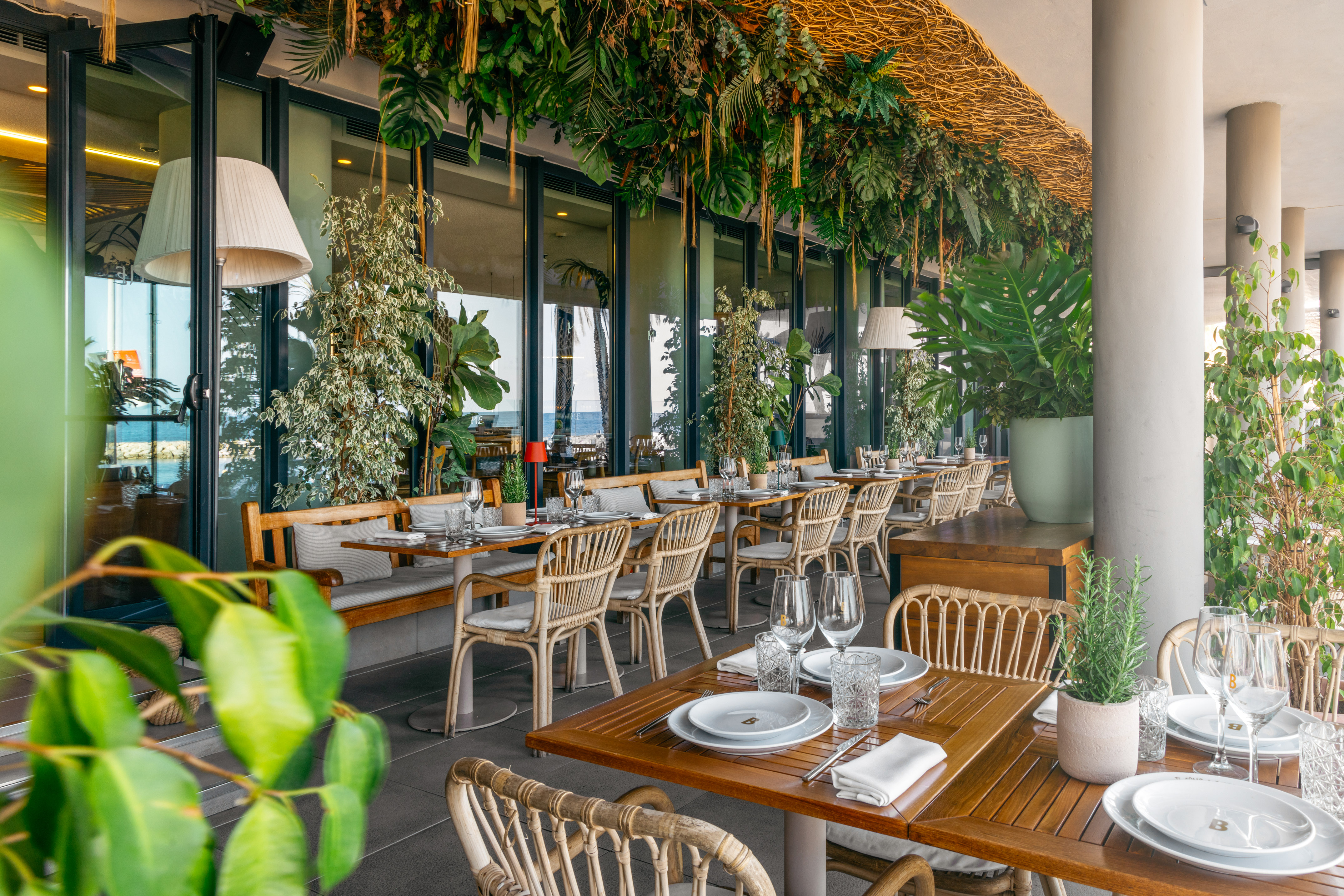 Tropical restaurant patio with lush greenery, wicker seating, and sea views.