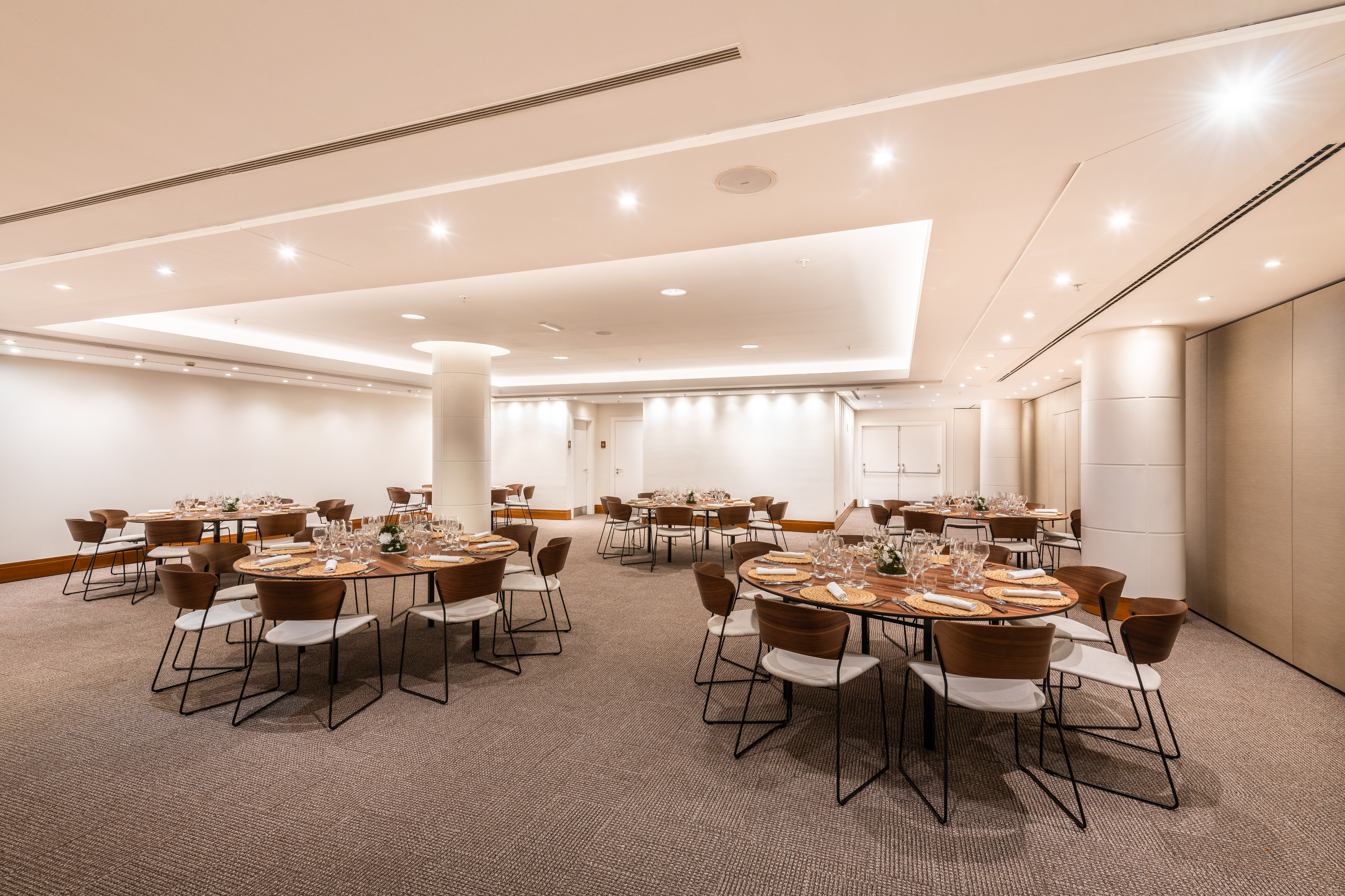 Modern event space with set round dining tables and chairs on carpet.