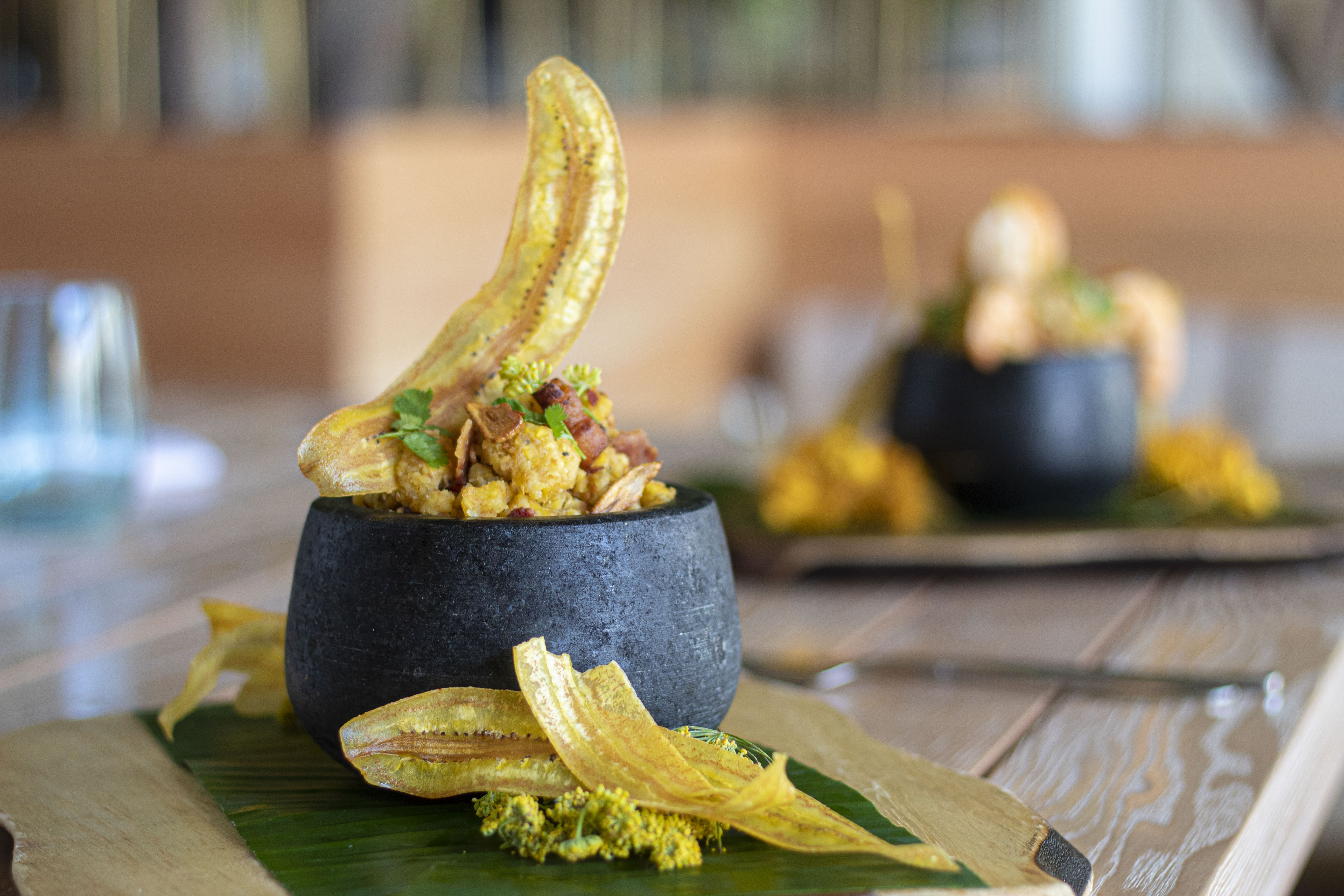 Mofongo with bacon and plantain chips in a dark stone bowl on a banana leaf.