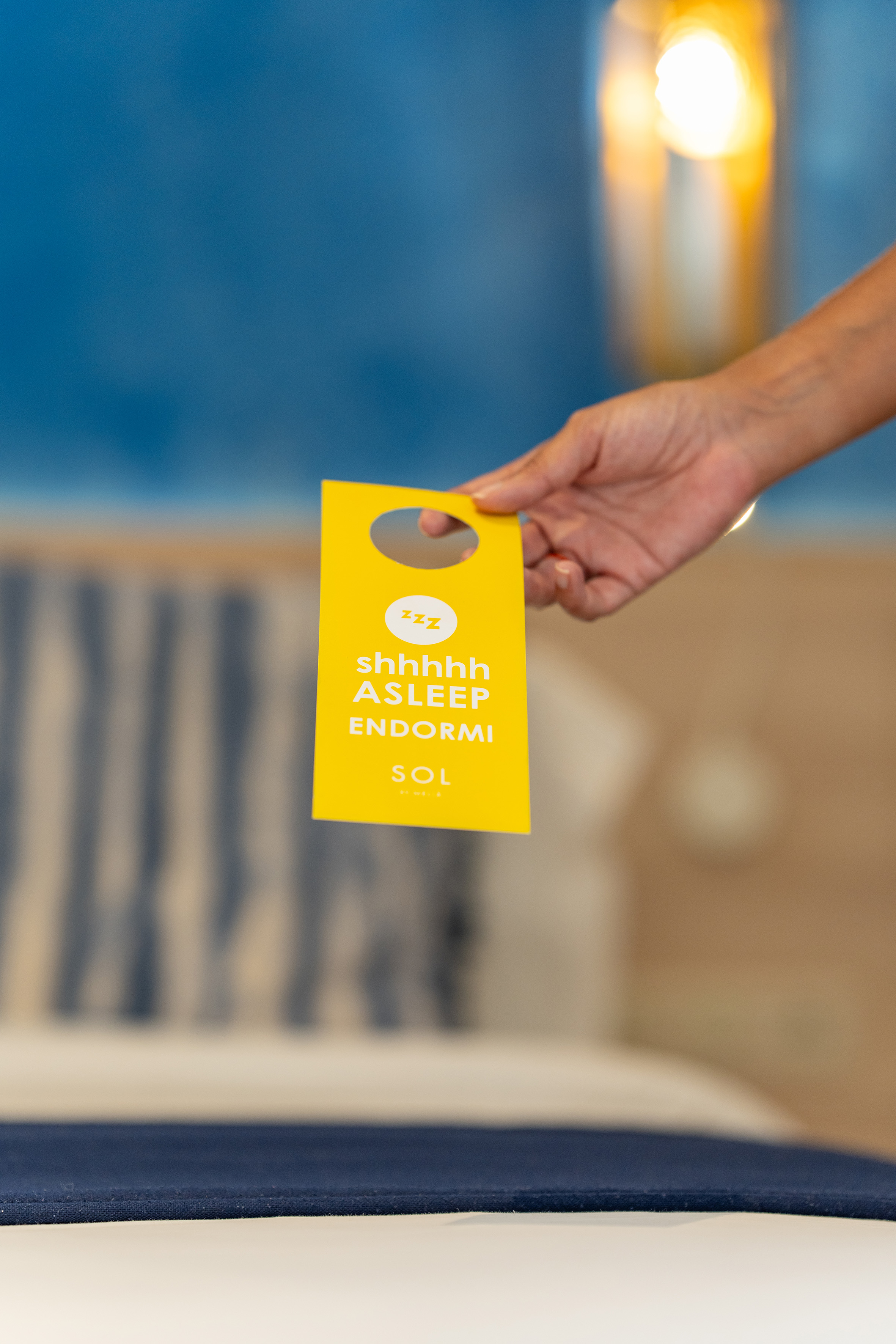 Hand holding a yellow "shhhhhh ASLEEP" hotel door hanger by Sol Hotels.