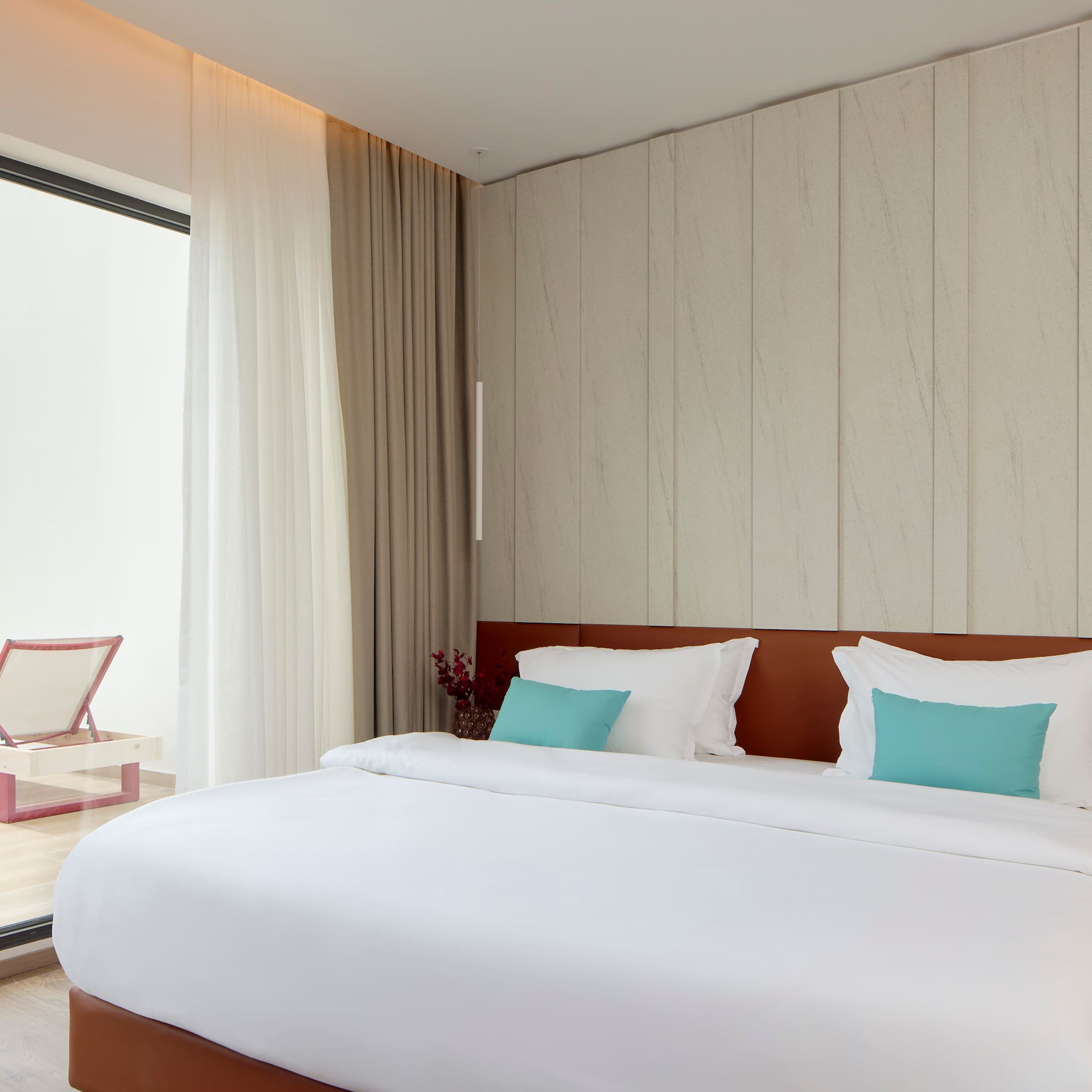 a bed with white sheets and blue pillows in a room with a glass door