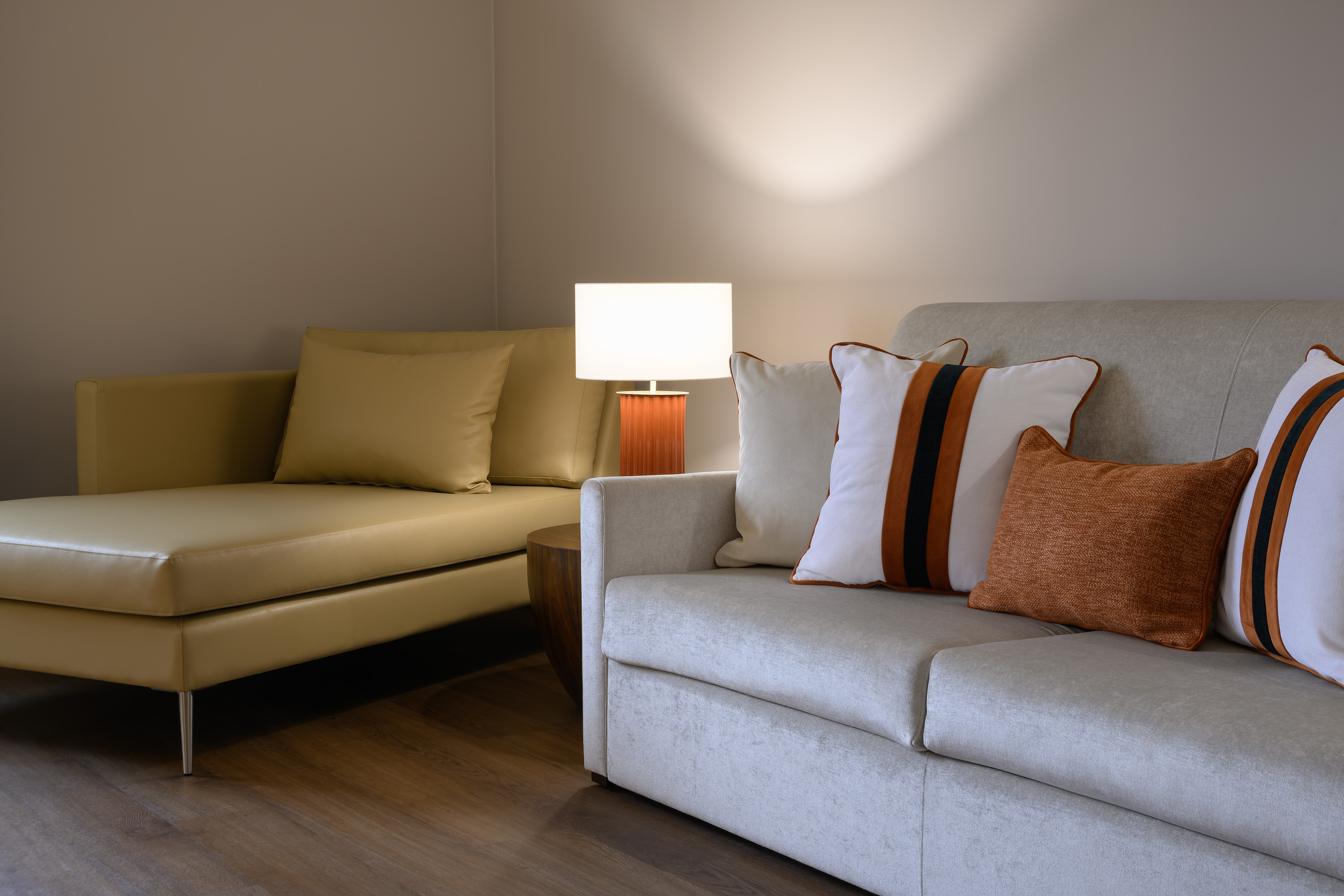 Modern living room with beige sofa, leather chaise, decorative pillows, and warm lamp.