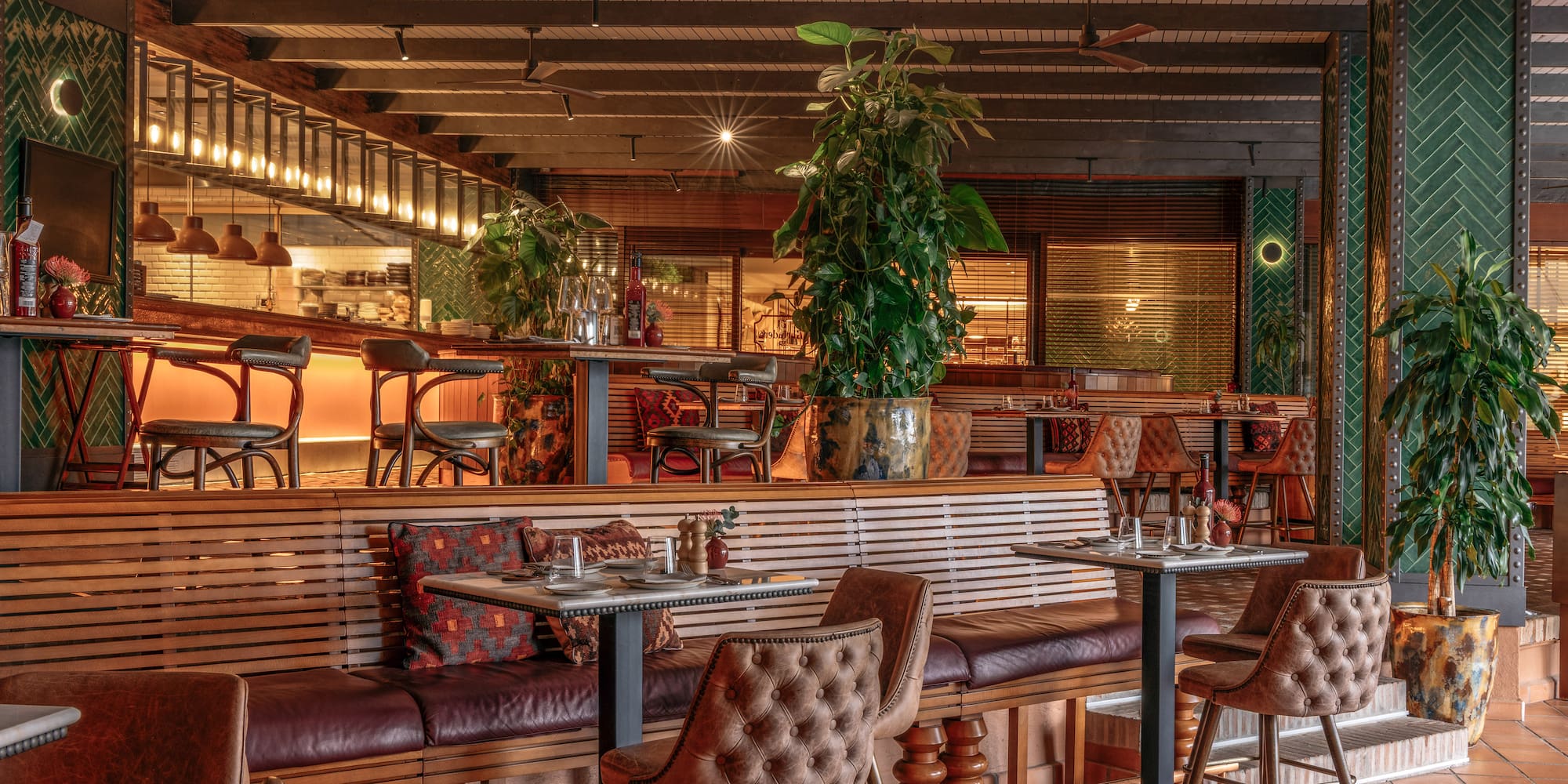 Modern restaurant interior with leather seating, wooden decor, and potted plants.