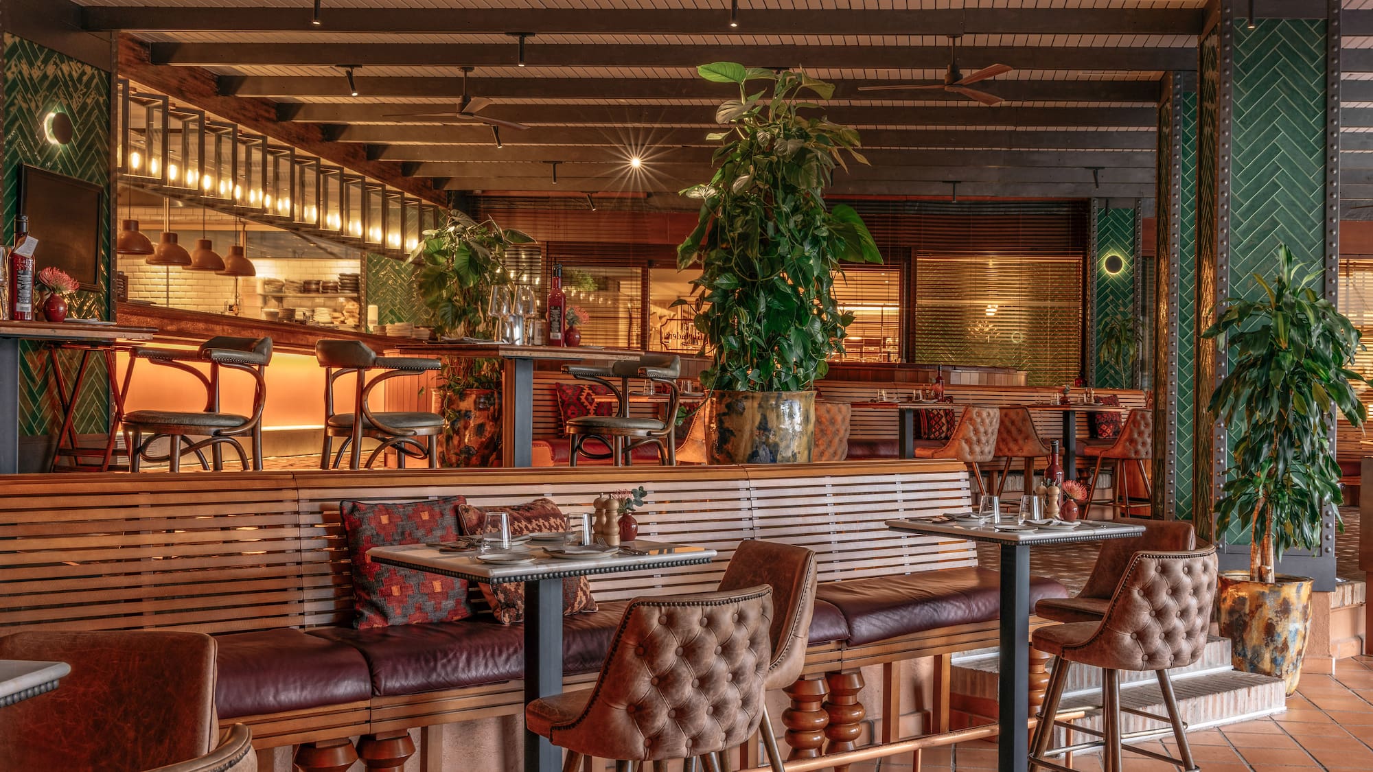 Modern restaurant interior with leather seating, wooden decor, and potted plants.