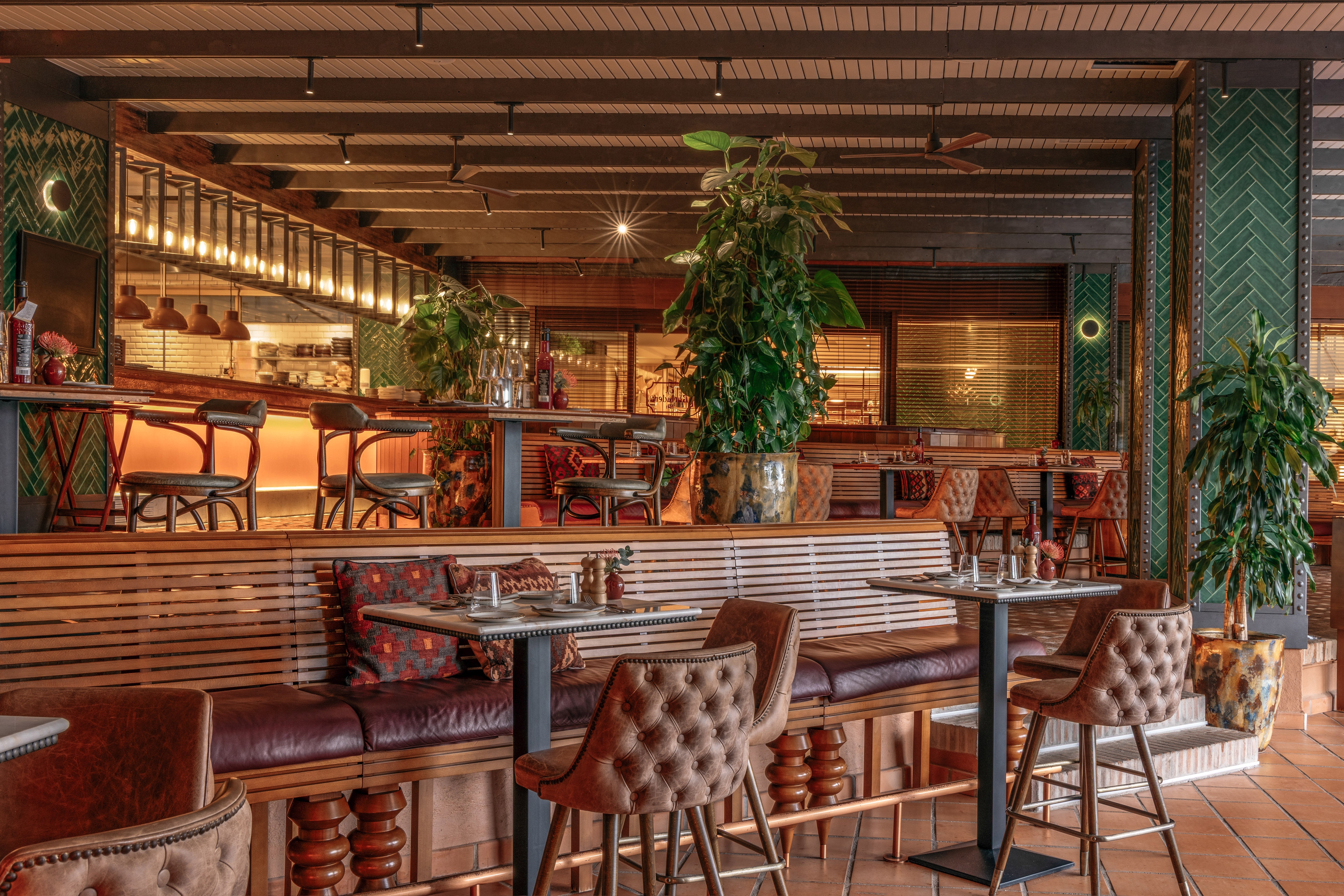 Modern restaurant interior with leather seating, wooden decor, and potted plants.