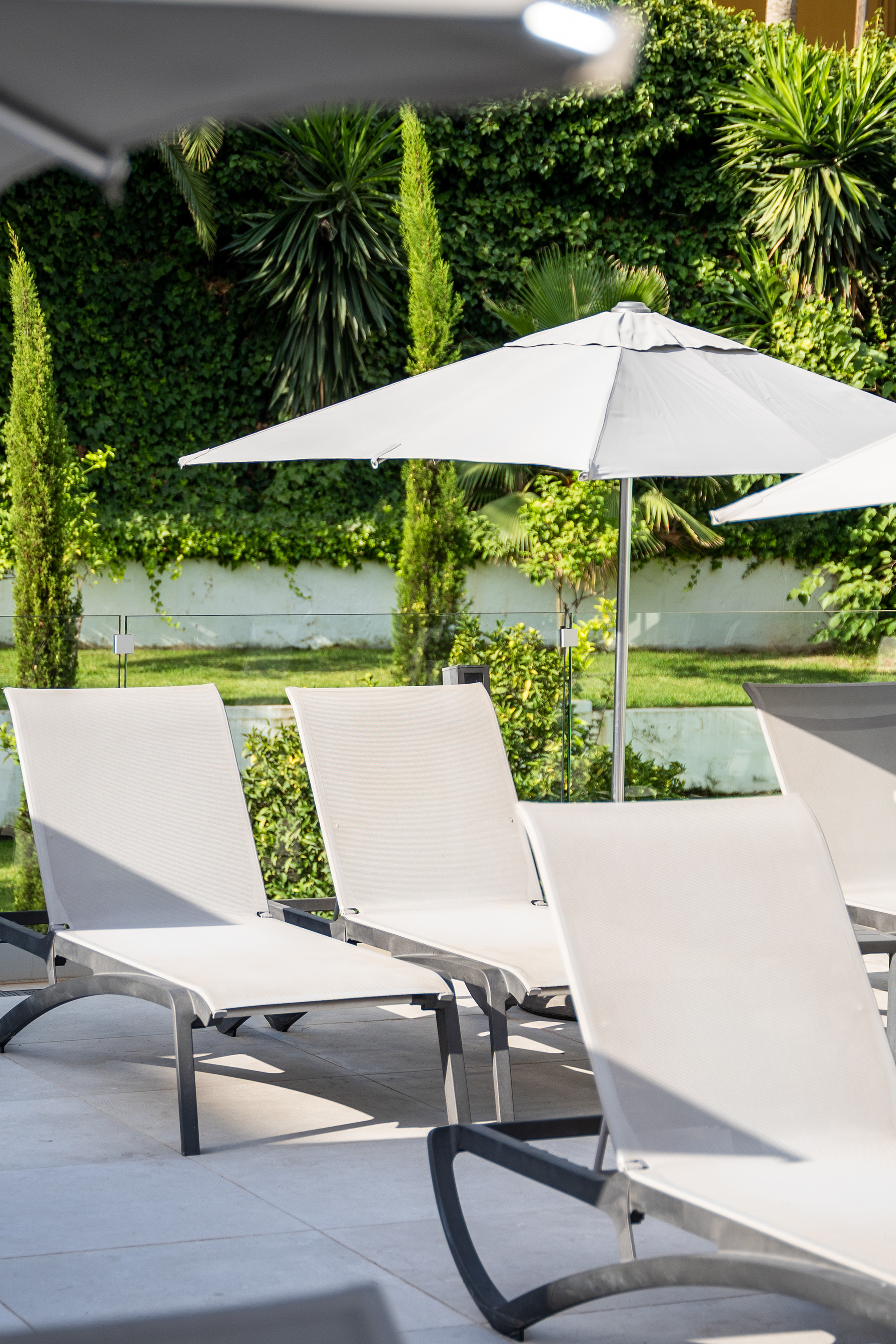 White sun loungers under a grey parasol in a resort poolside lounge.