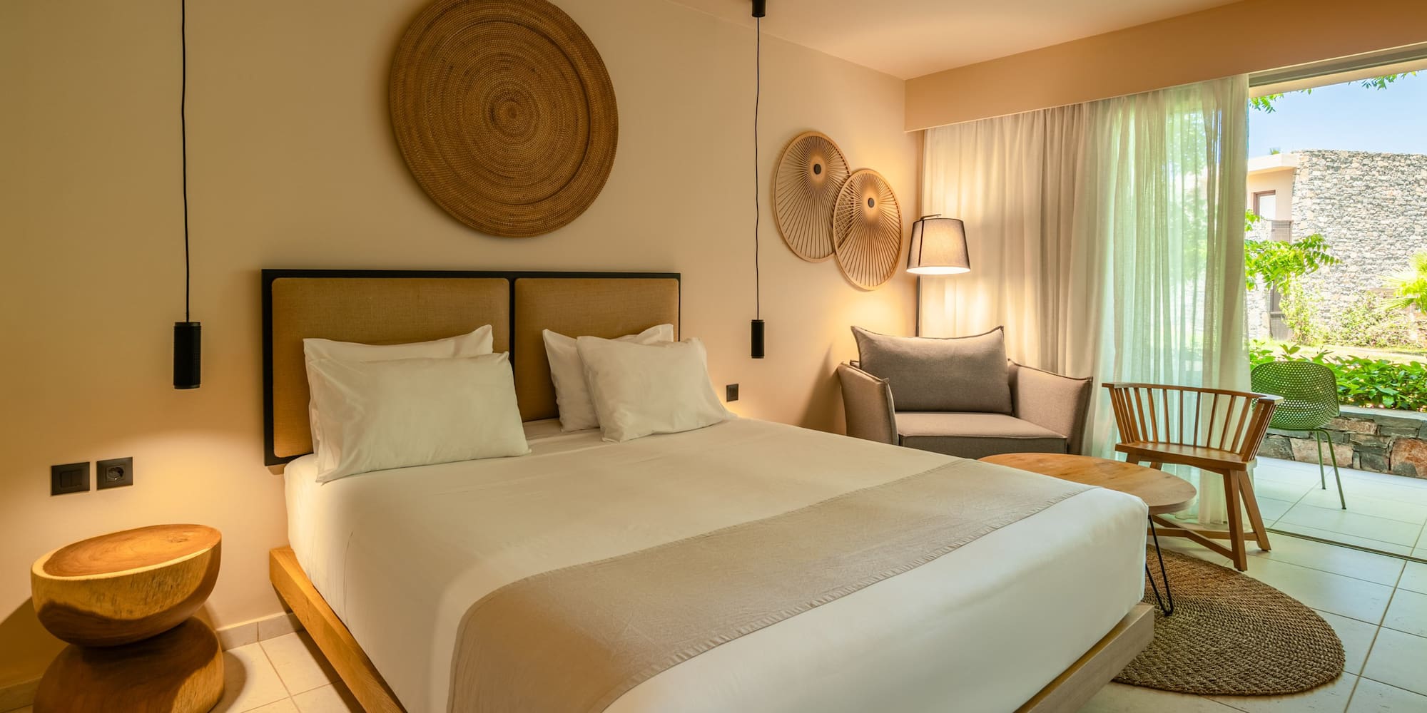 Modern hotel bedroom with king bed, natural decor, sitting area, and patio.