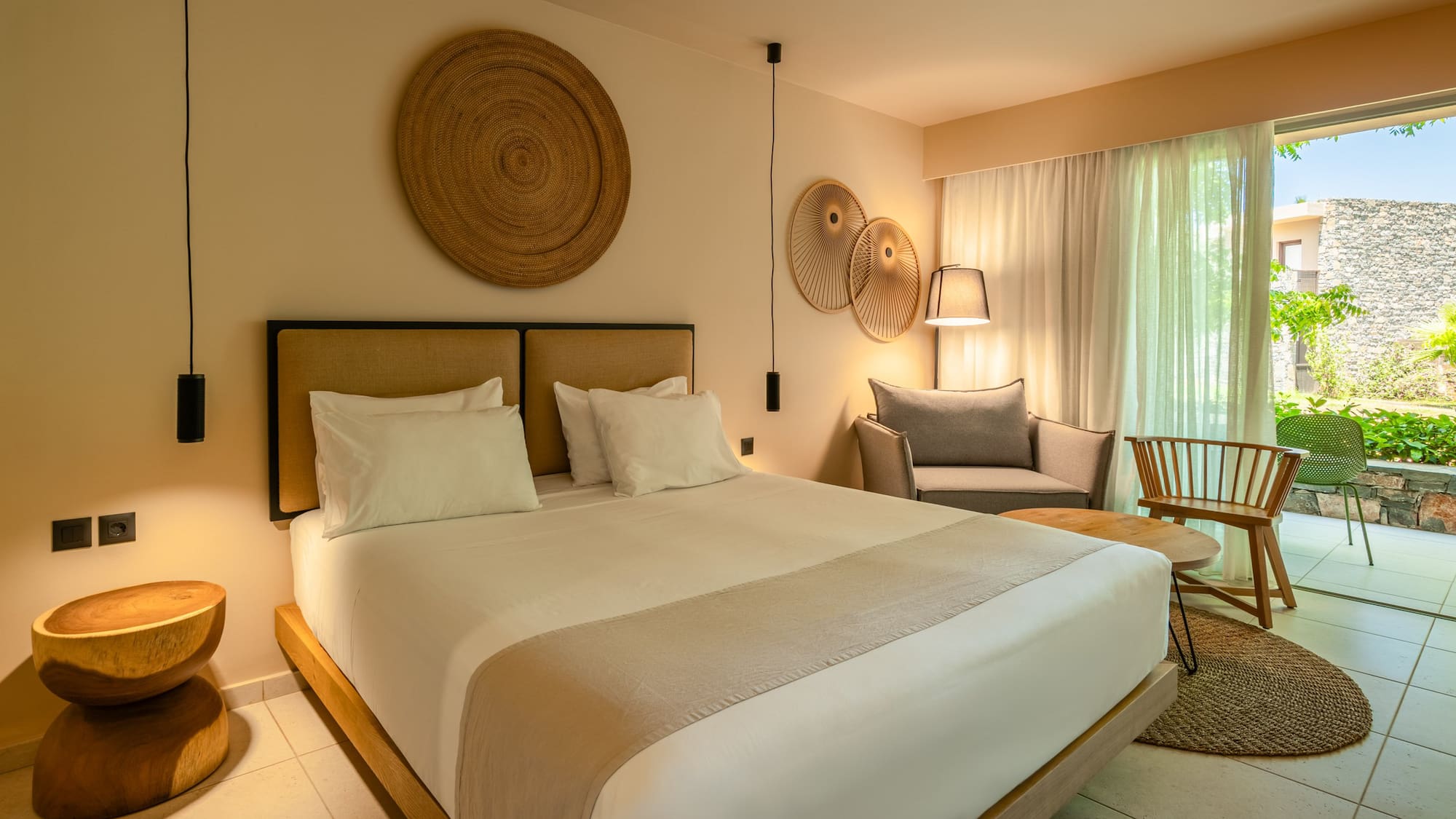 Modern hotel bedroom with king bed, natural decor, sitting area, and patio.