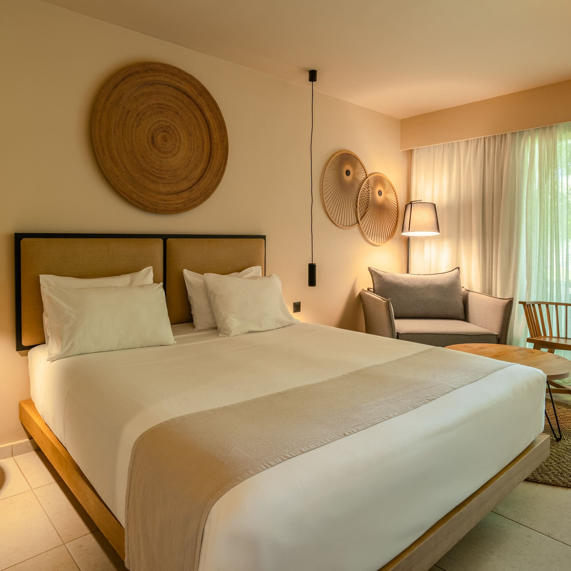 Modern hotel bedroom with king bed, natural decor, sitting area, and patio.