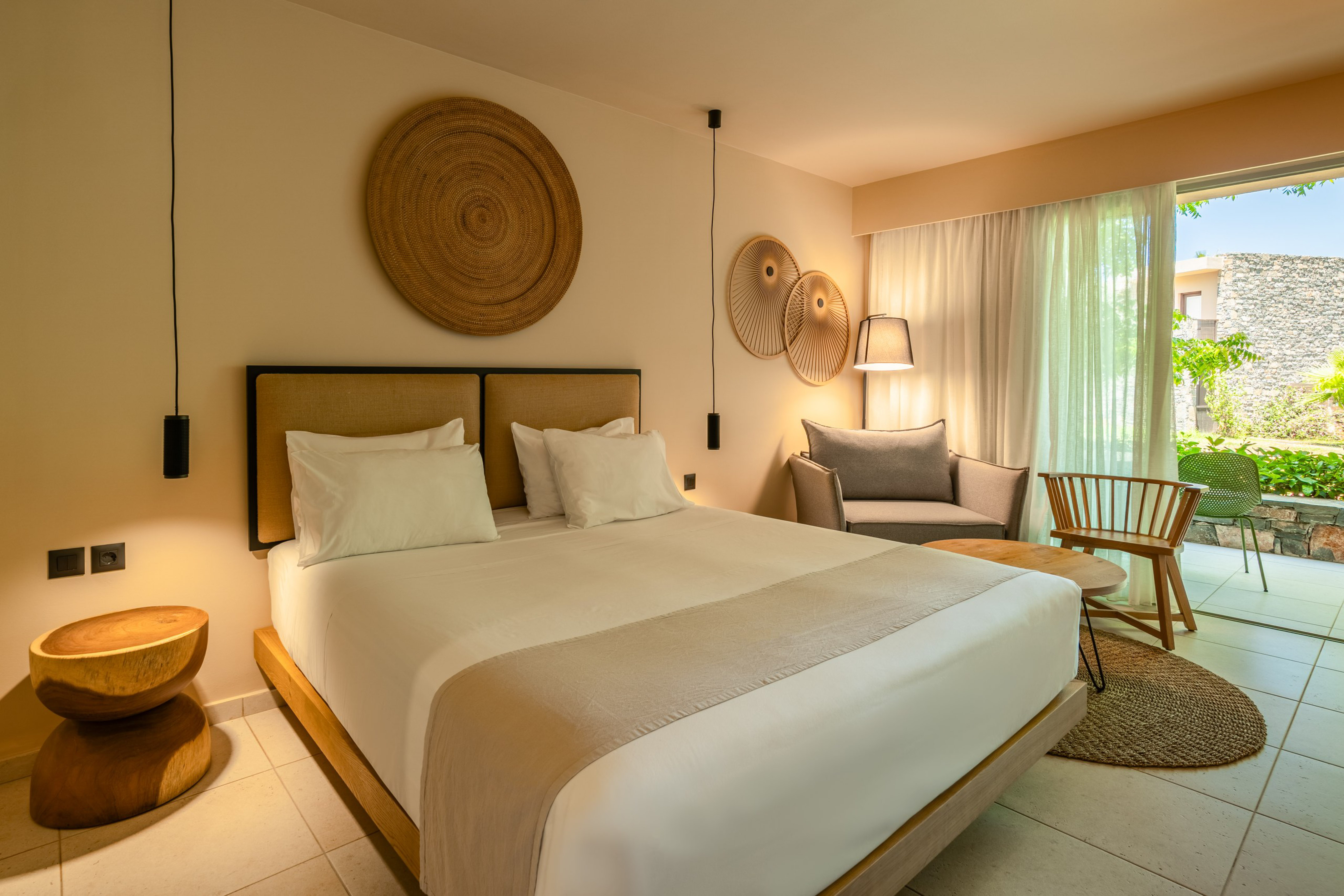 Modern hotel bedroom with king bed, natural decor, sitting area, and patio.