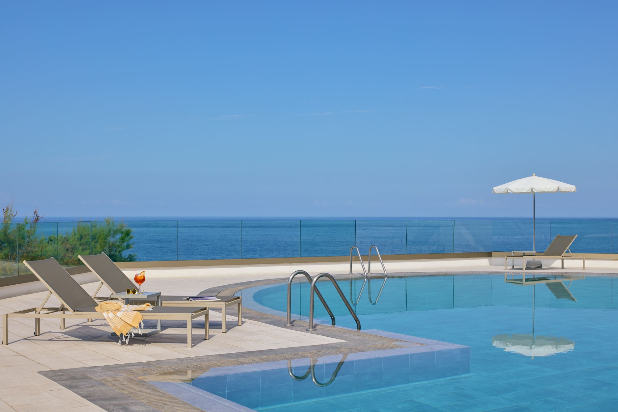 Oceanfront resort swimming pool with lounge chairs, cocktail, and blue ocean view.