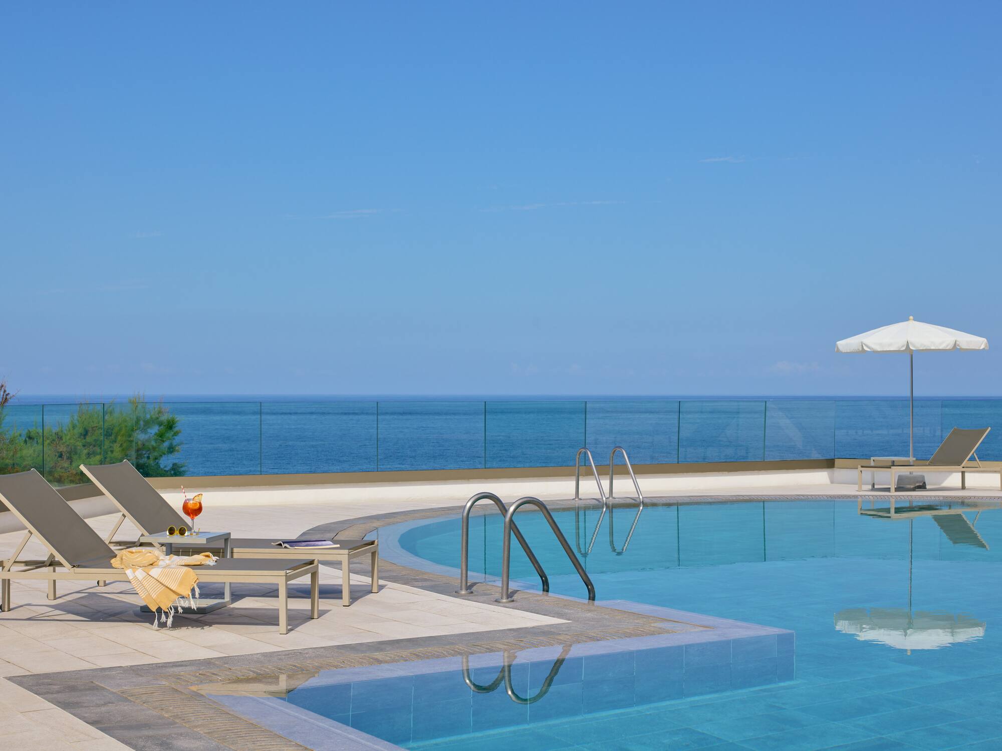a pool with chairs and umbrellas by the ocean
