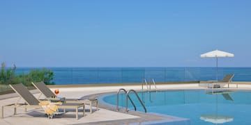 a pool with chairs and umbrellas by the ocean