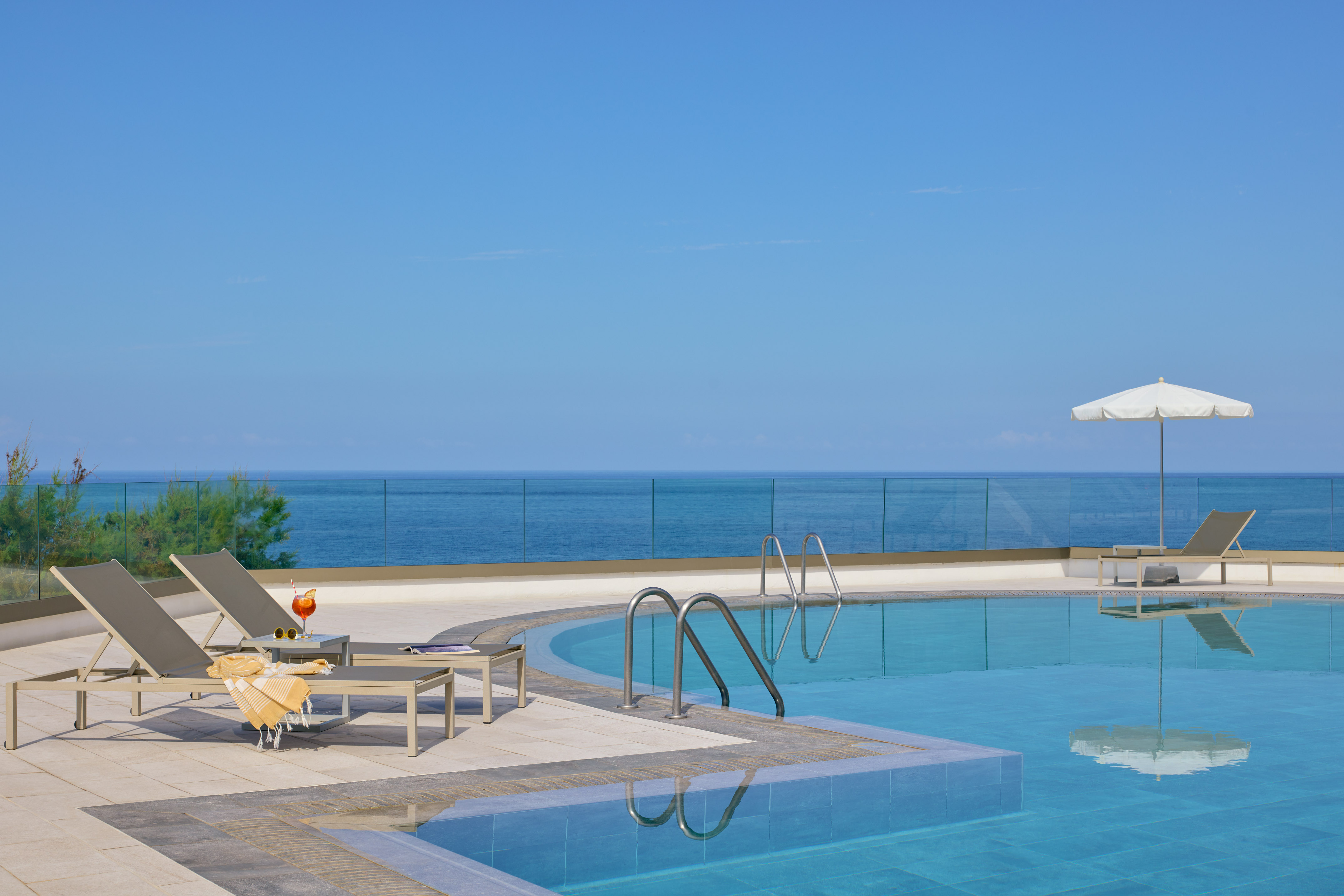 Oceanfront resort swimming pool with lounge chairs, cocktail, and blue ocean view.