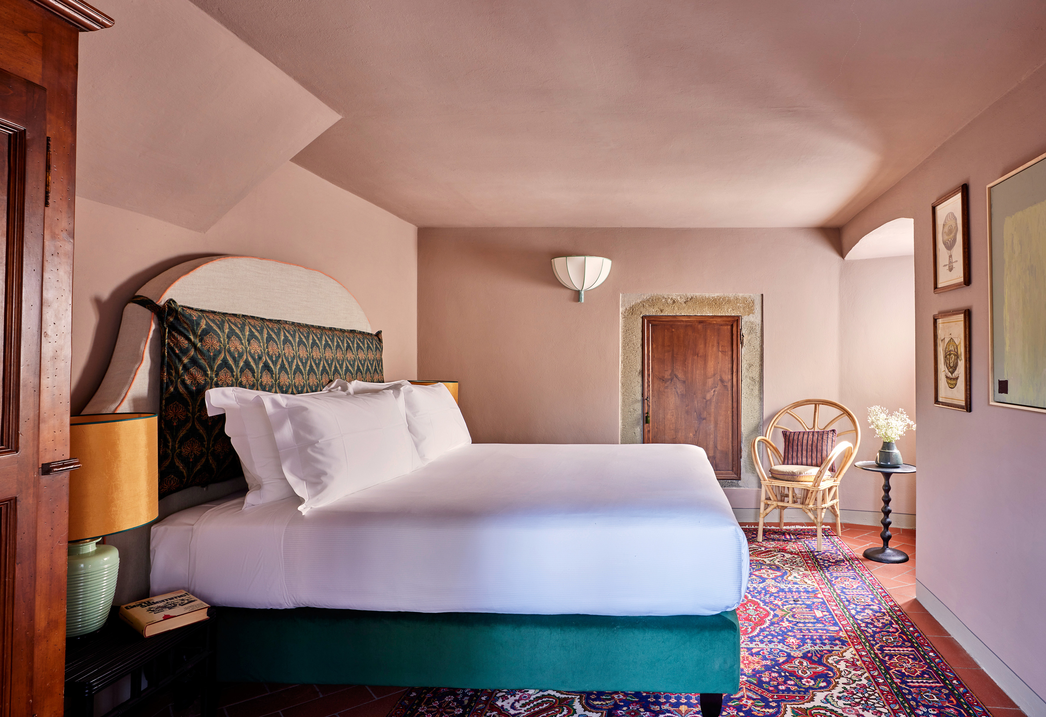 Luxurious European hotel bedroom with patterned rug, green bed, and pink walls.