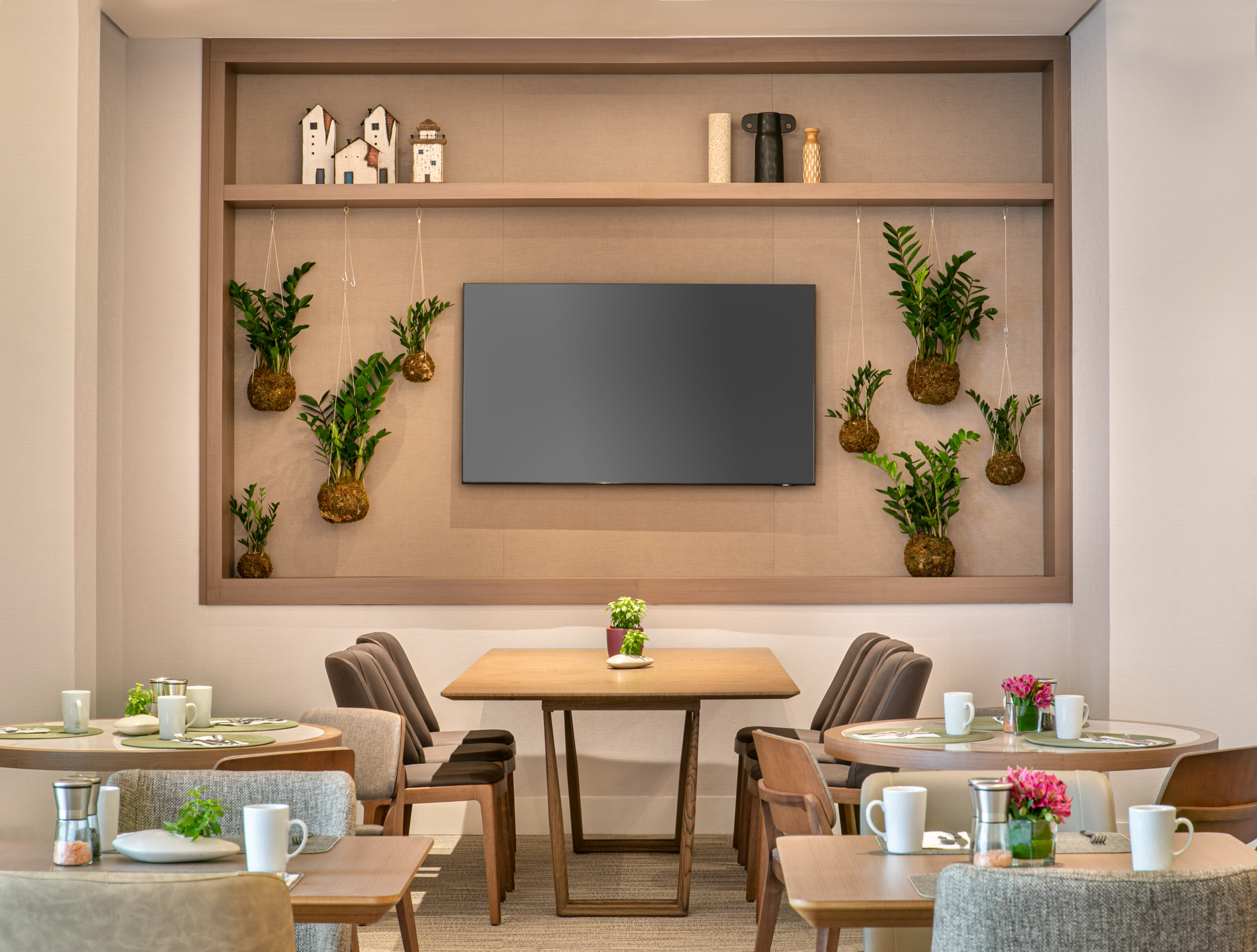 Modern restaurant dining room with wooden tables, comfortable chairs, and decorative plants.
