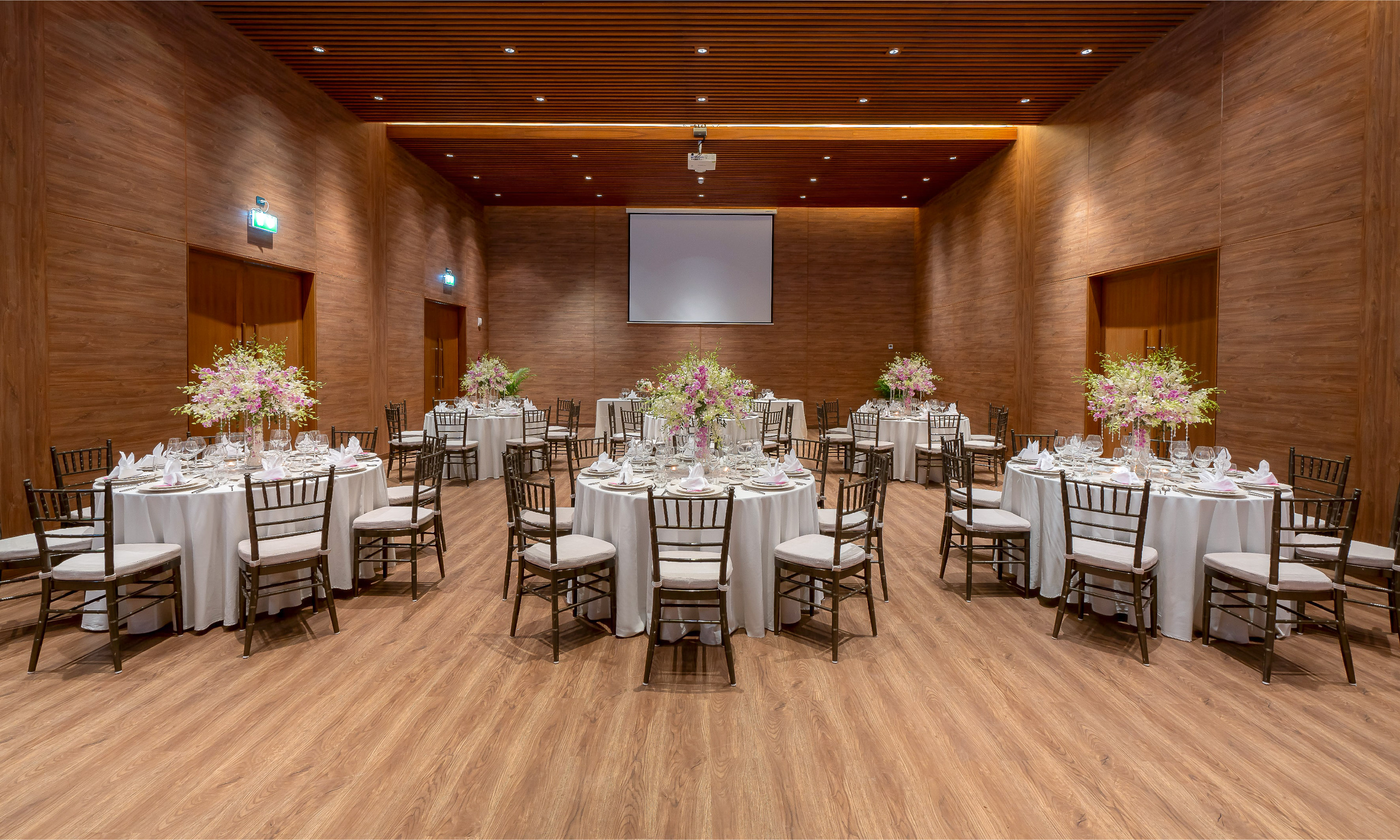 Wood-paneled banquet hall with elegant table settings and projector screen.