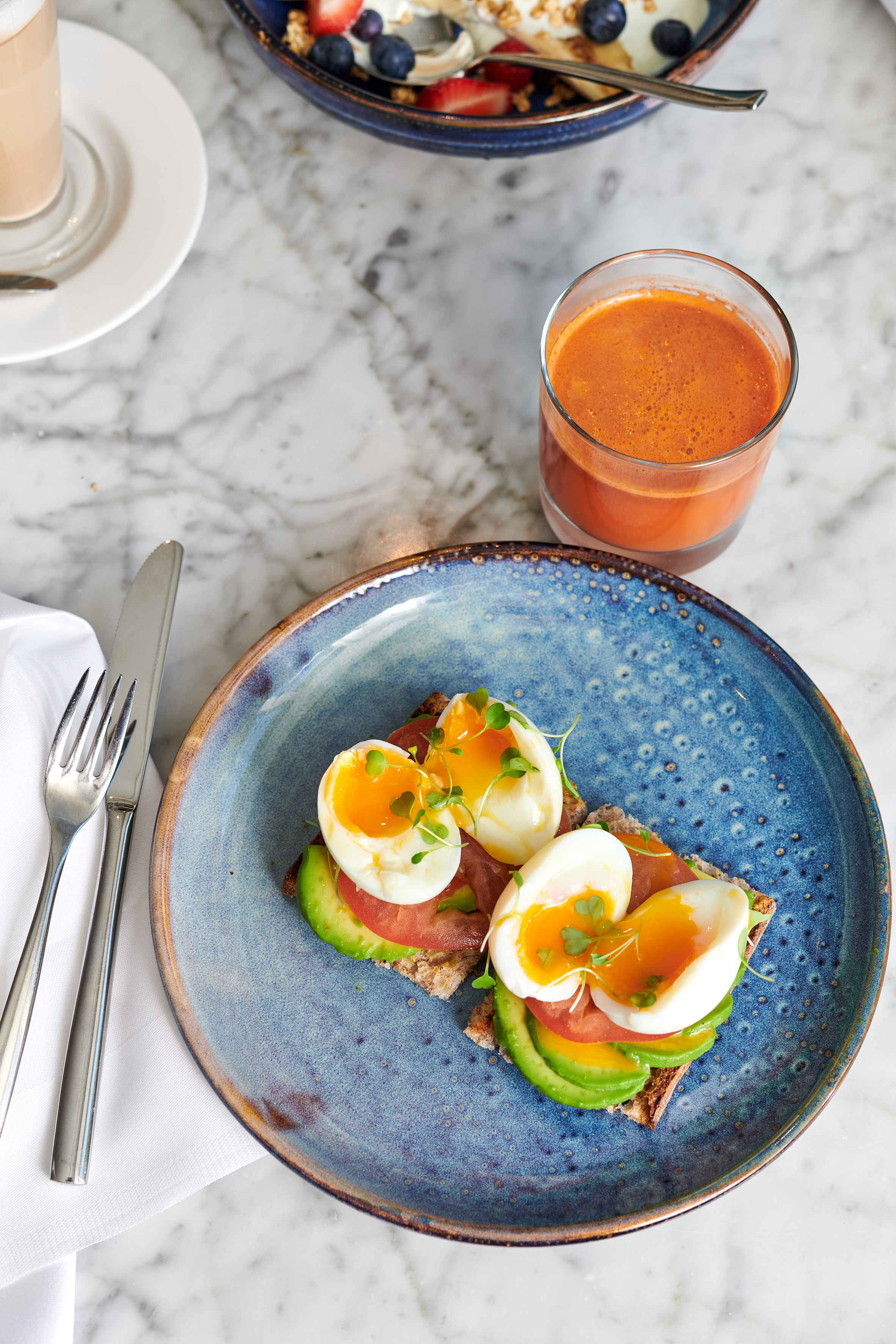 Soft-boiled eggs and avocado toast breakfast with orange juice on marble.