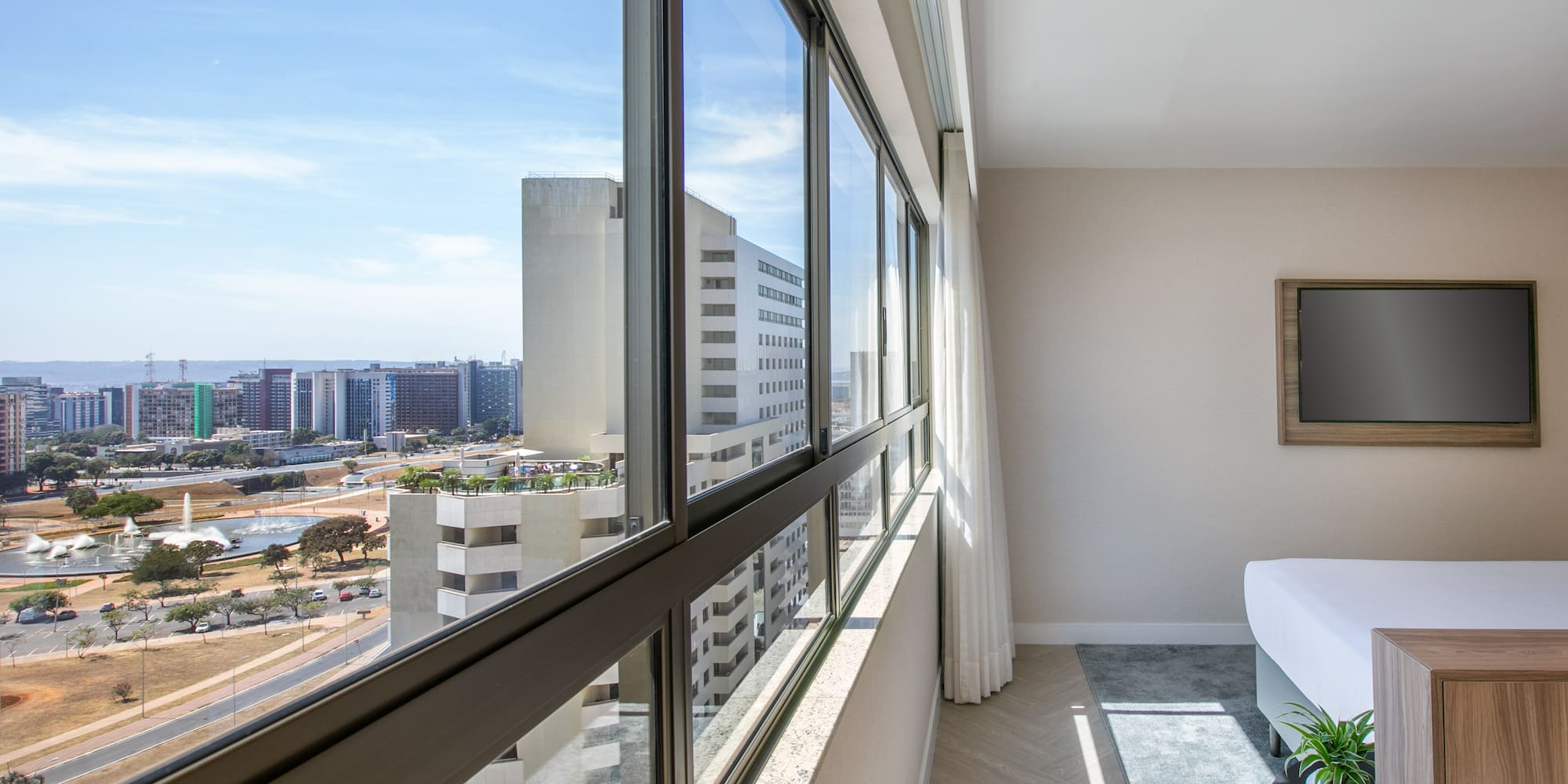 Modern hotel room with panoramic city view through expansive windows.