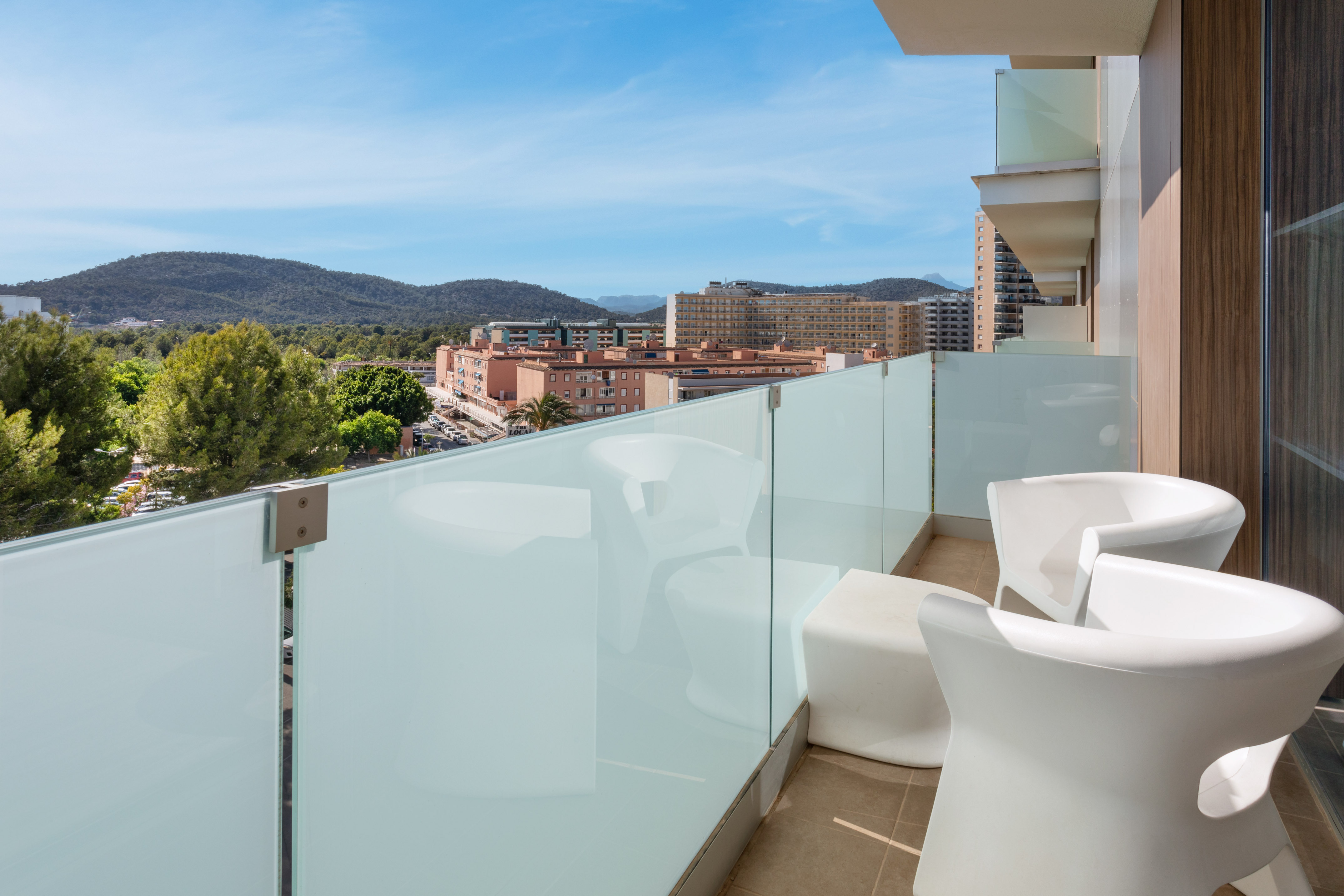 Modern hotel balcony with white furniture and city mountain view.
